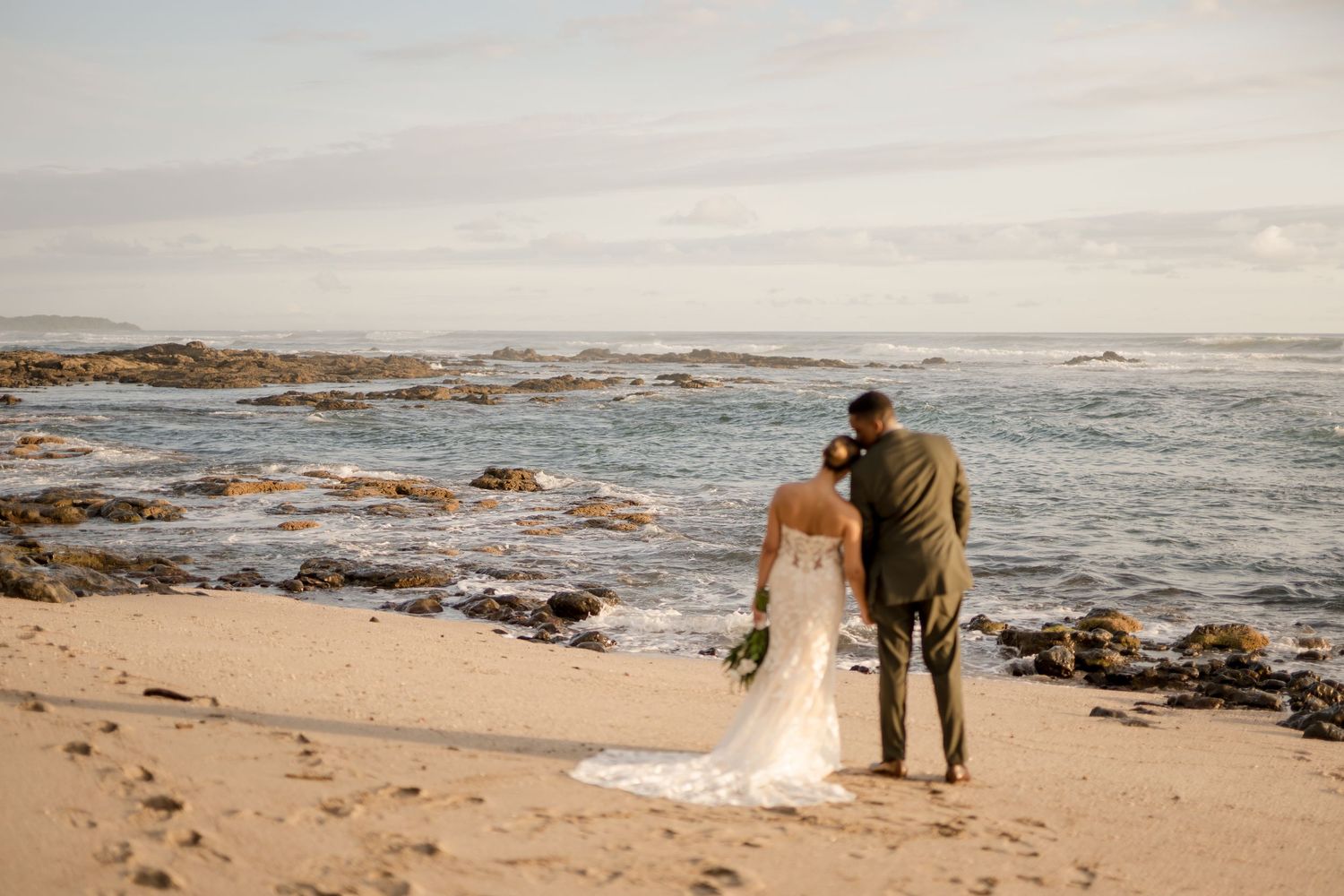 Couple walking hand in hand along Costa Rica's rocky shoreline after their destination wedding ceremony in Playa Langosta, Guanacaste.