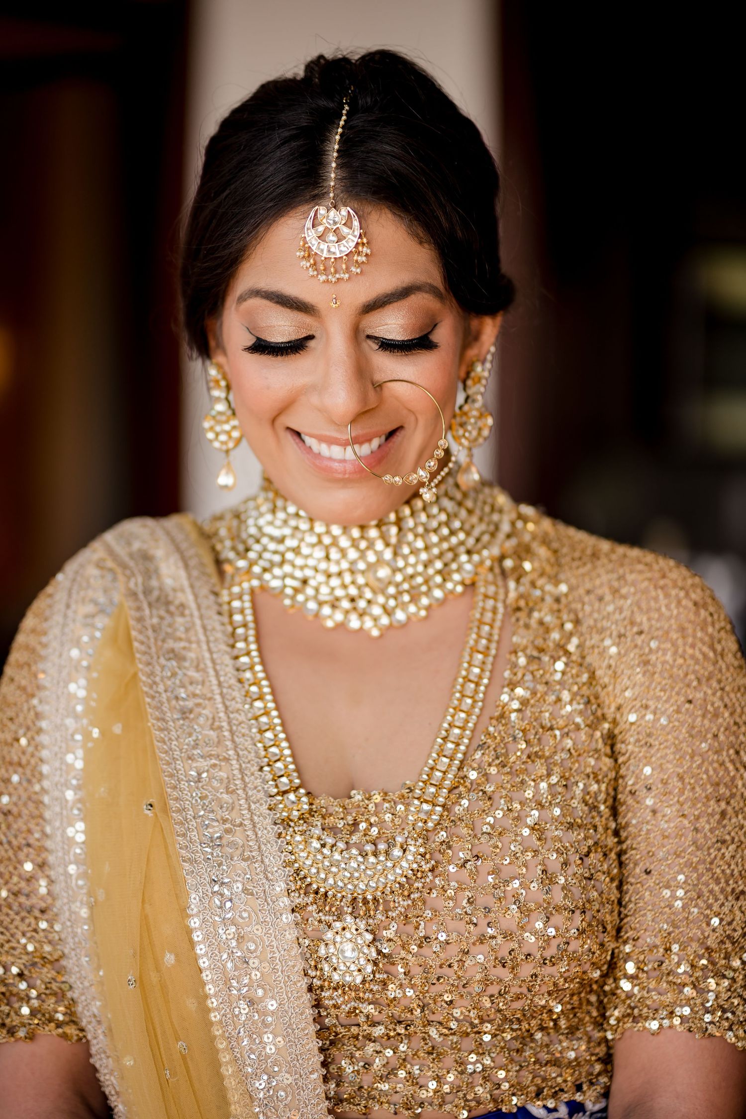 South Asian bride wearing traditional gold bridal jewelry and embroidered wedding attire during a luxury multicultural celebration.