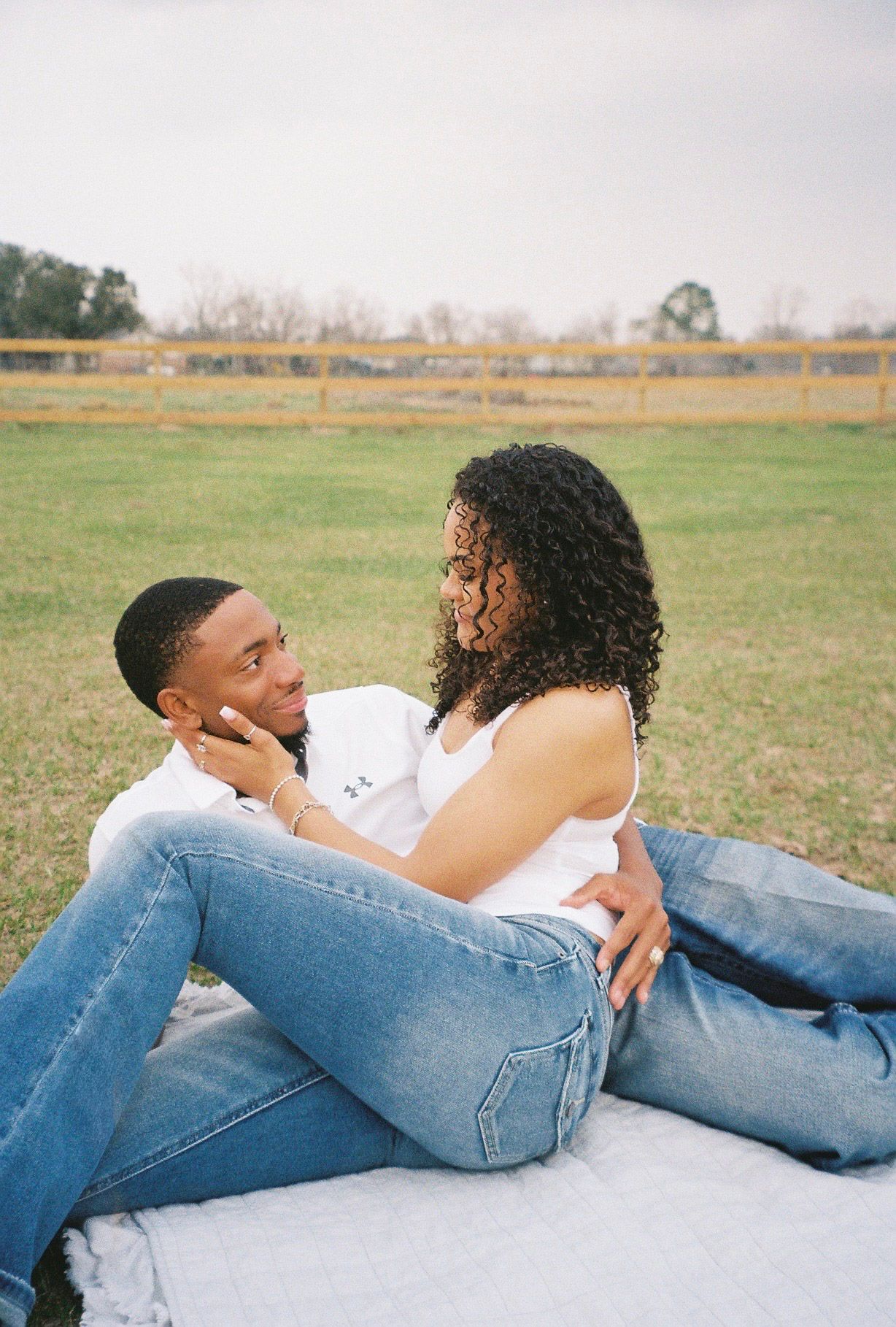 Couple in casual denim outfits sharing a tender moment while relaxing on a blanket in a field.