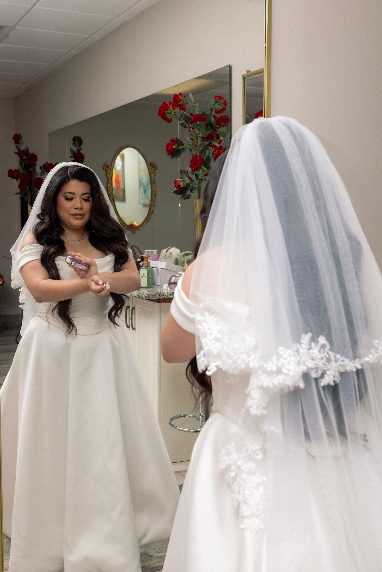 Bride in white wedding gown and lace veil admiring her reflection in a bridal salon mirror.