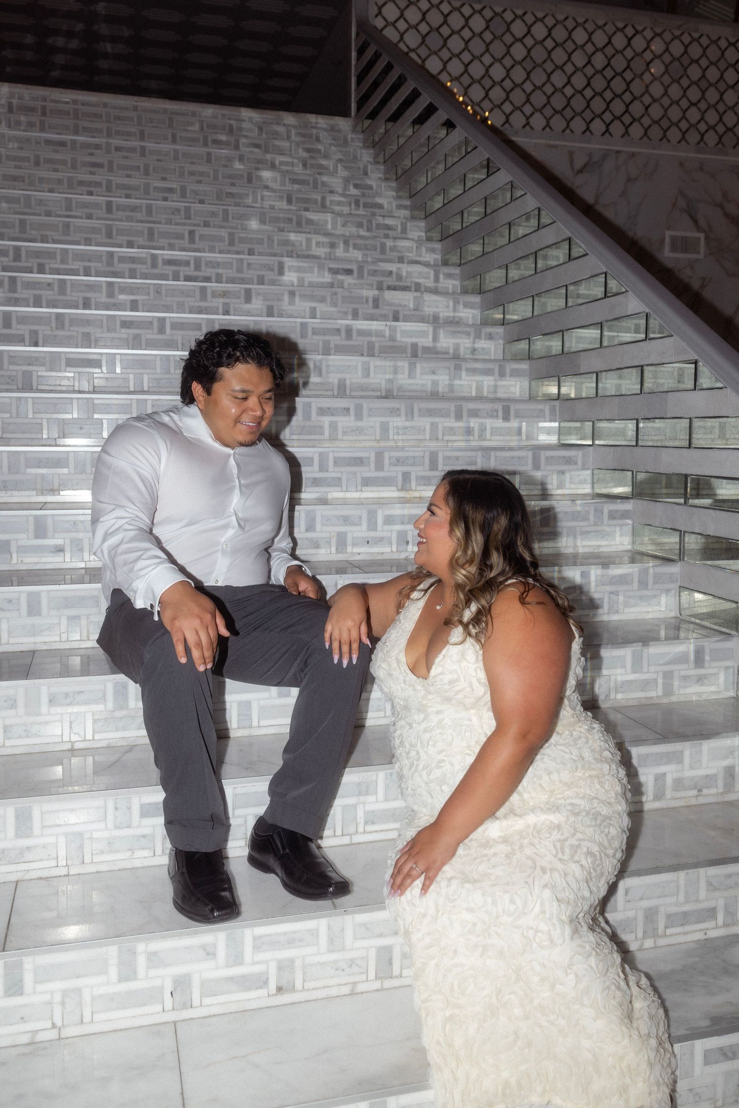 Bride and groom sitting on elegant marble stairs, sharing a romantic moment during their wedding reception.