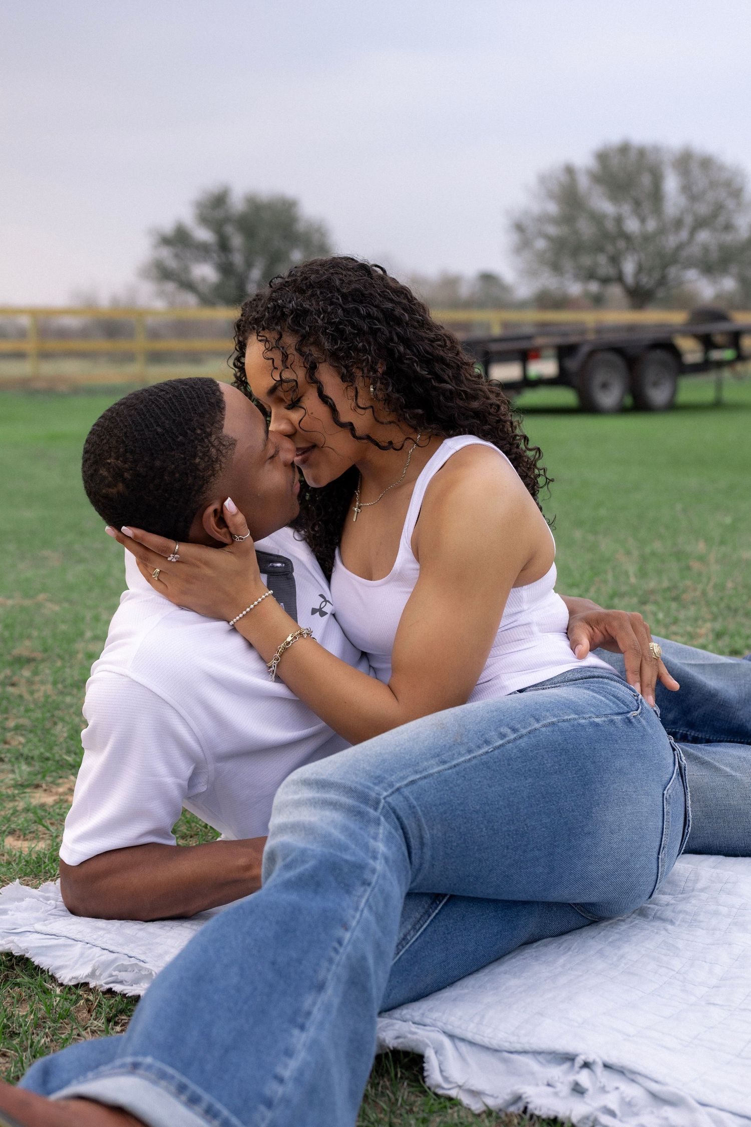 Young couple sharing a romantic kiss while sitting on blanket in green grassy field.
