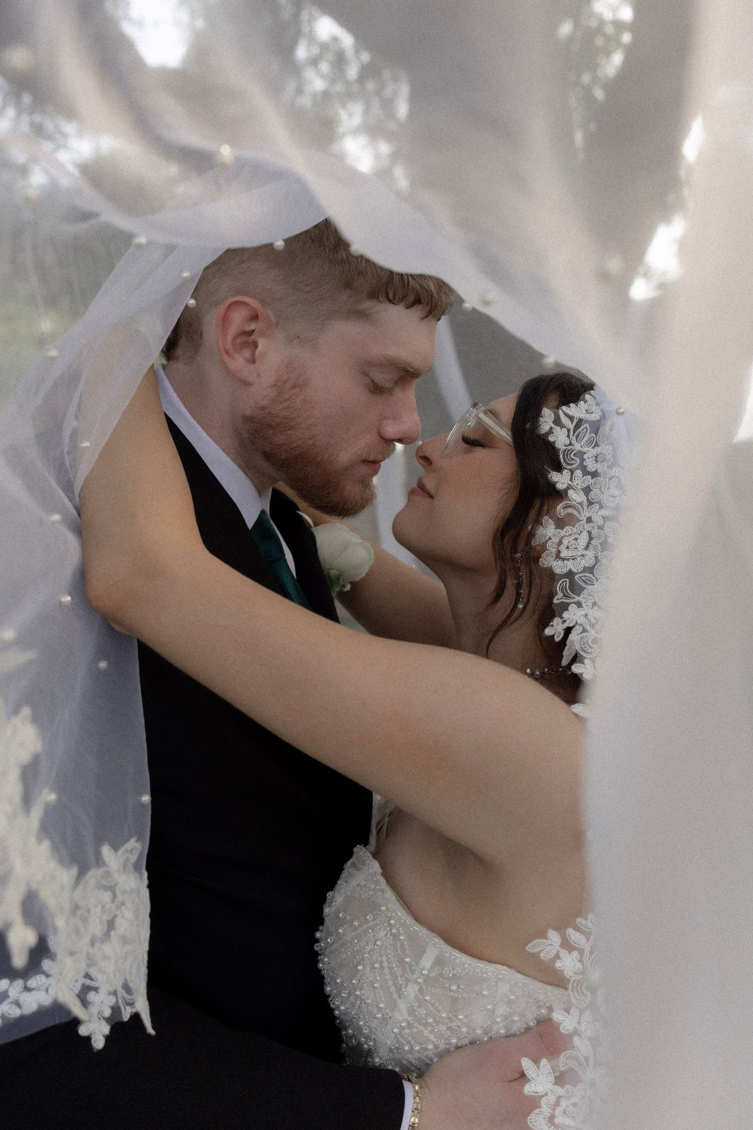 Bride and groom share an intimate moment under a lace wedding veil outdoors.