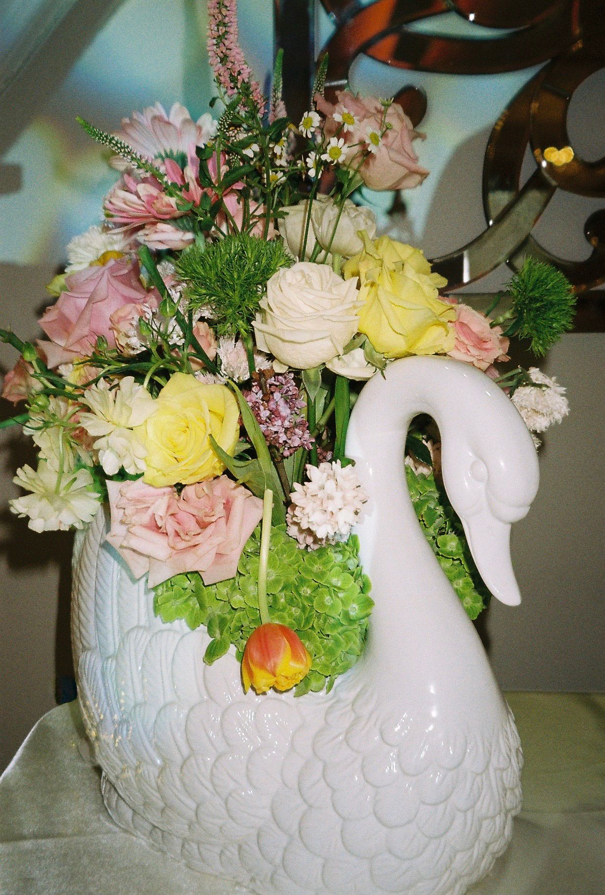 Elegant white ceramic swan vase filled with pink, yellow, and white spring flower arrangement.