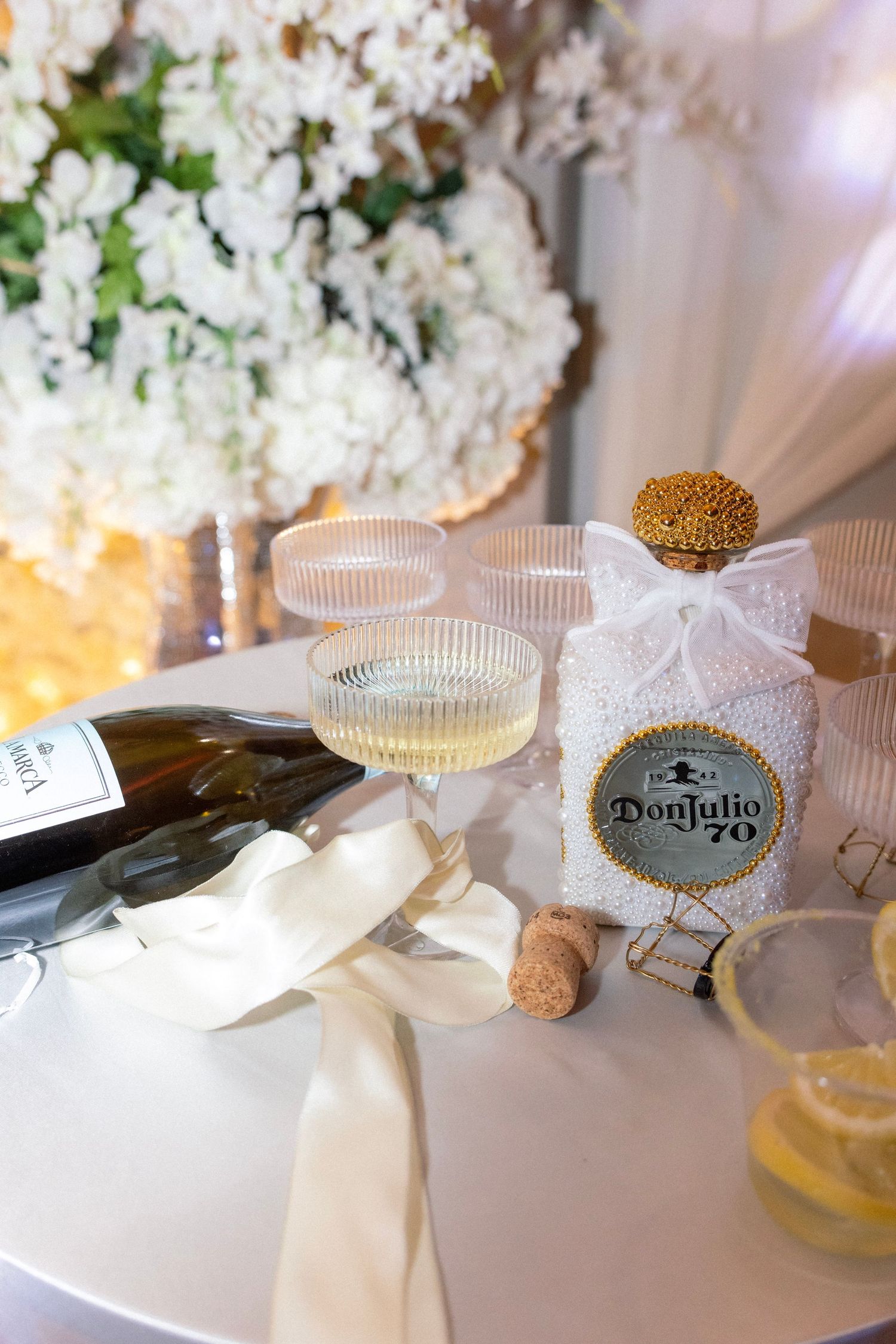 Don Julio 70 tequila bottle with champagne flutes and wine bottle on elegant white wedding reception table.