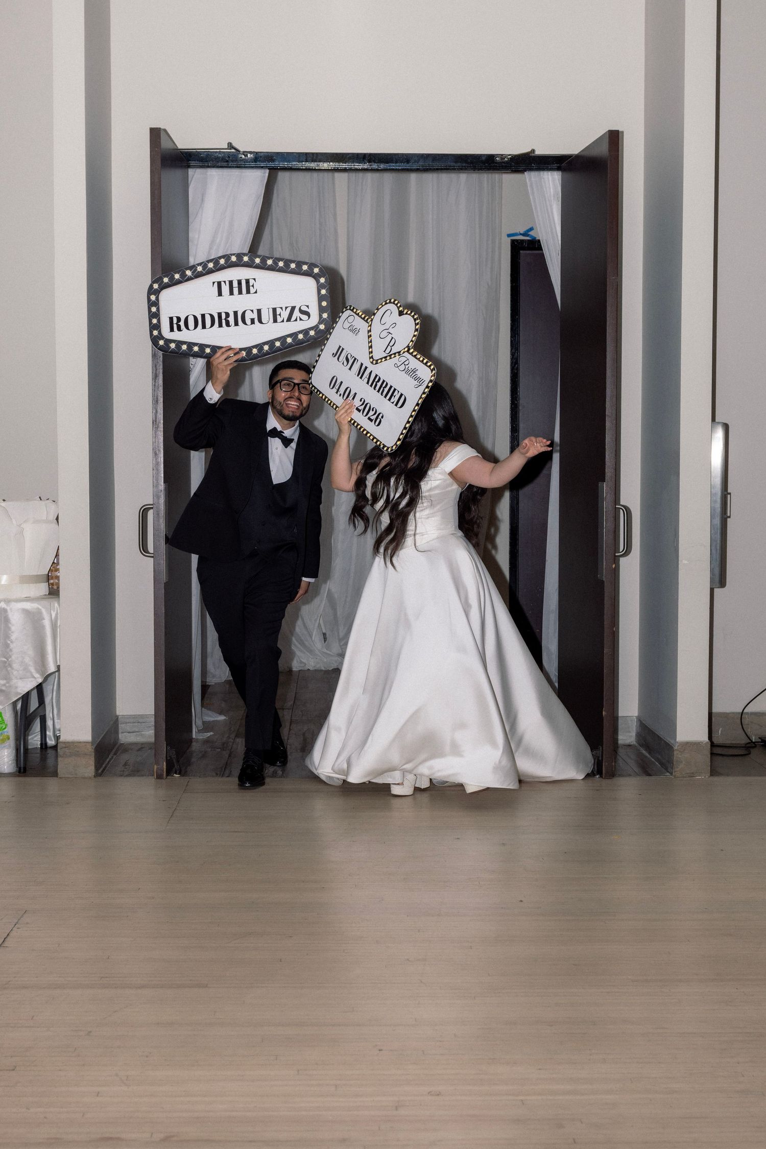 Newlywed couple posing with fun photo booth signs reading The Rodriguezes and Just Married at their wedding reception.