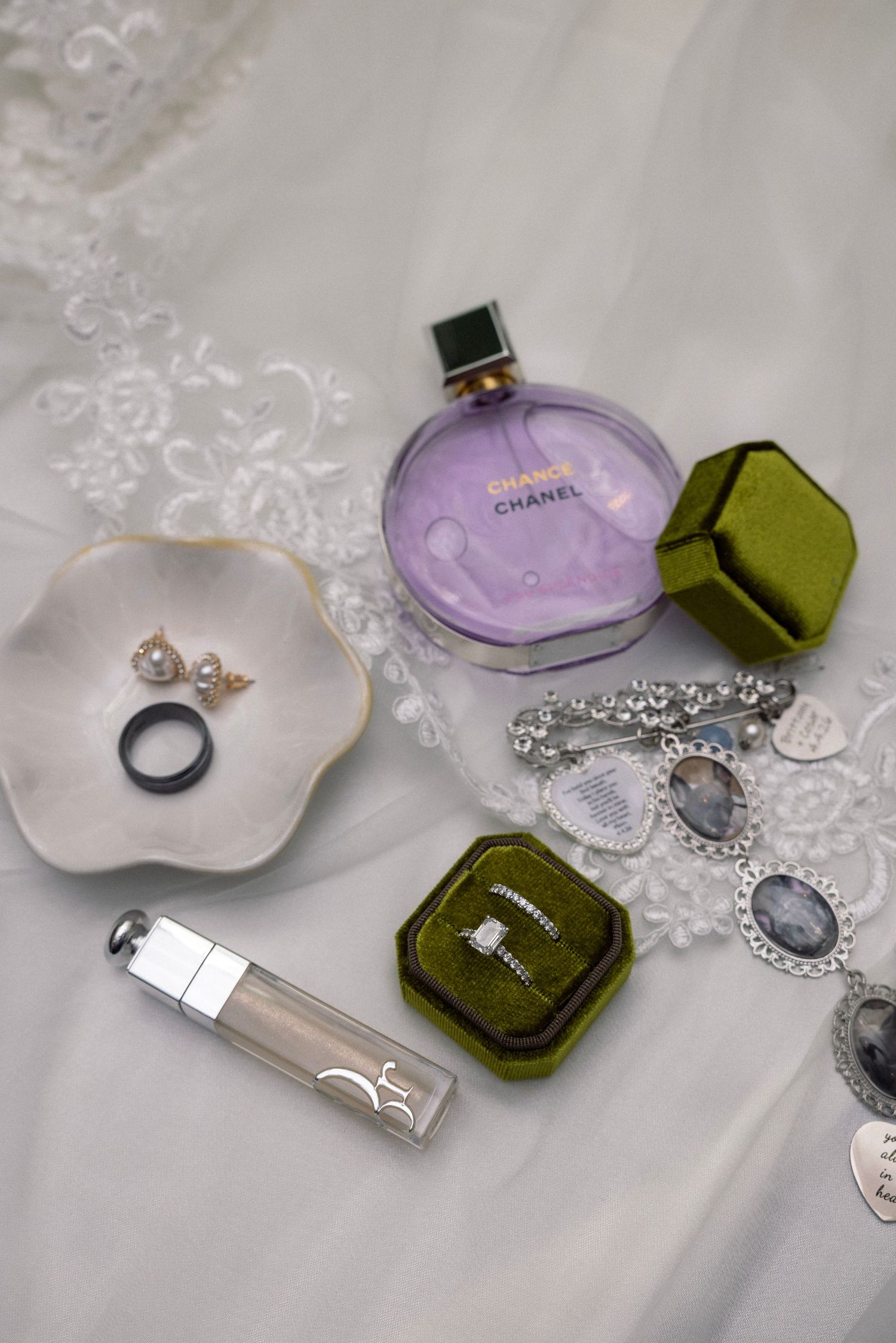 Elegant bridal flat lay featuring Chanel Chance perfume, diamond engagement ring in green velvet box, Dior lip gloss, and pearl earrings.