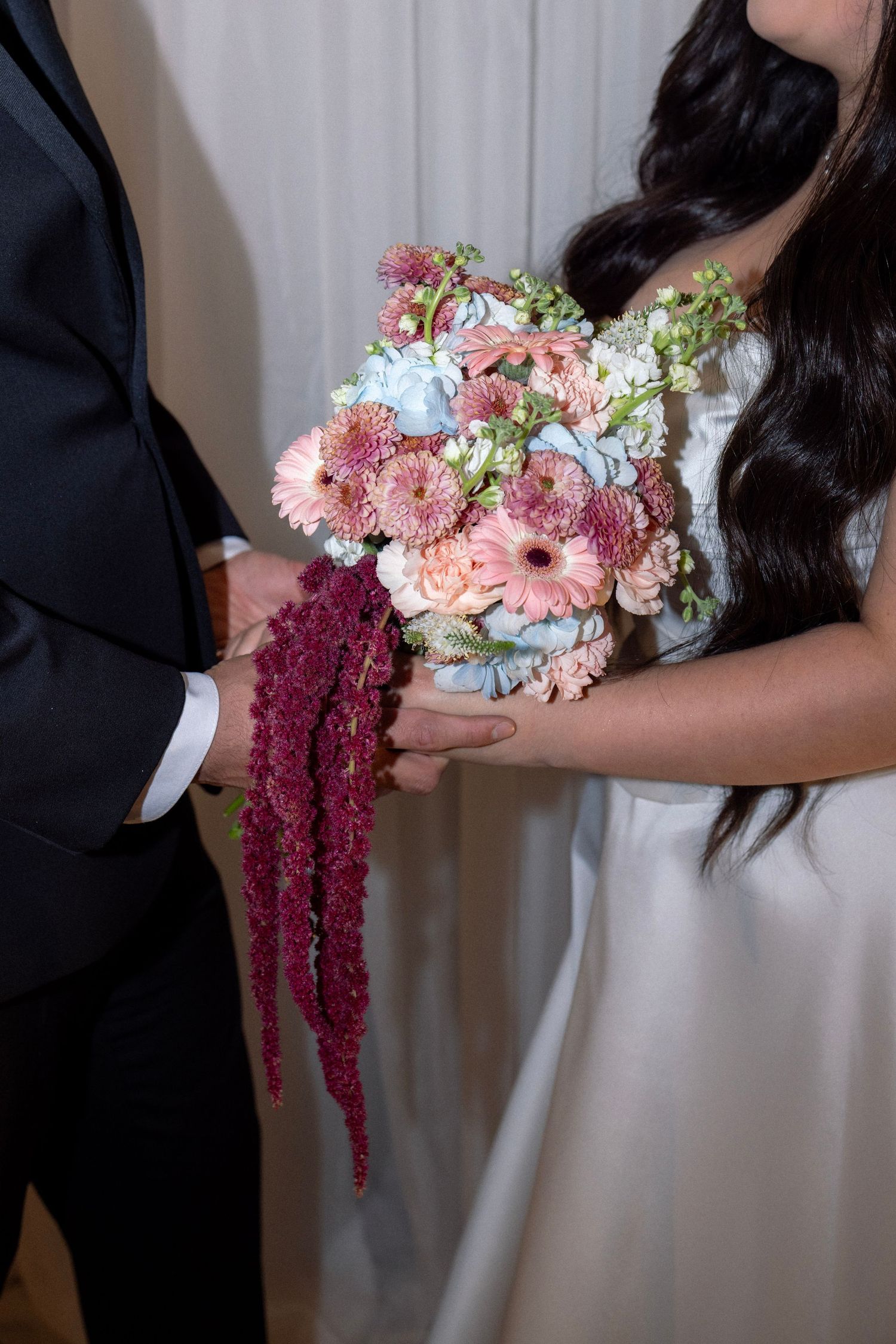 Close-up of bride holding colorful wedding bouquet with pink gerberas and burgundy amaranthus flowers.