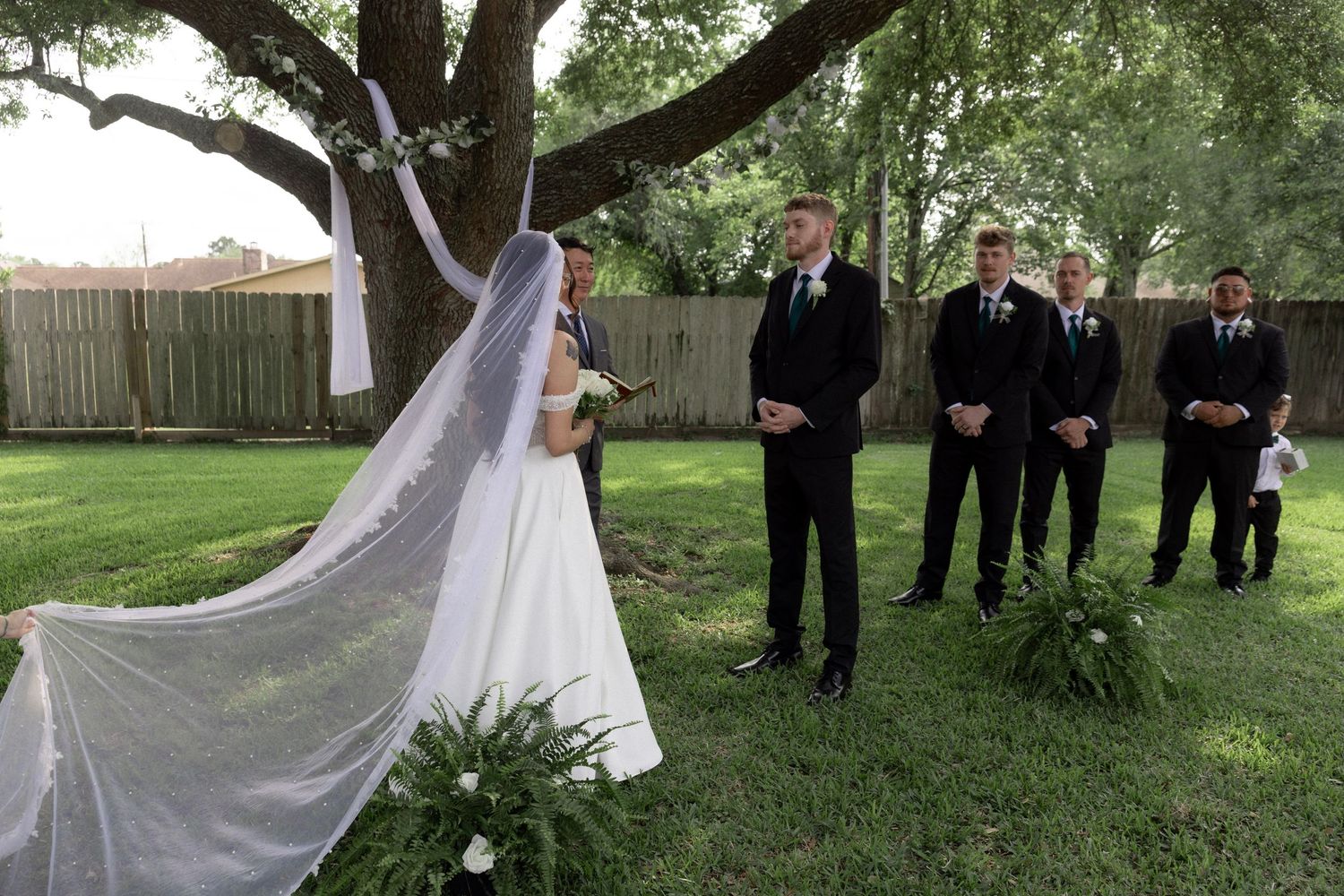 A bride and groom share a first look moment with groomsmen standing nearby outdoors.