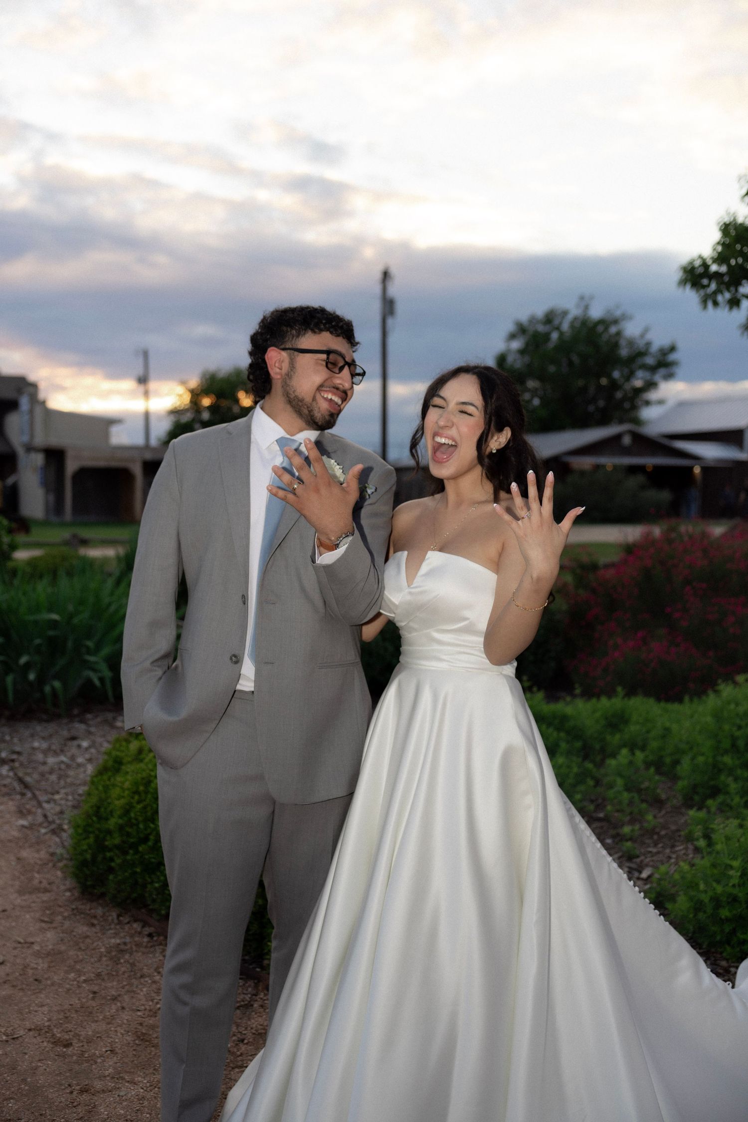 Laughing newlyweds display wedding rings outdoors at dusk after sunset ceremony.
