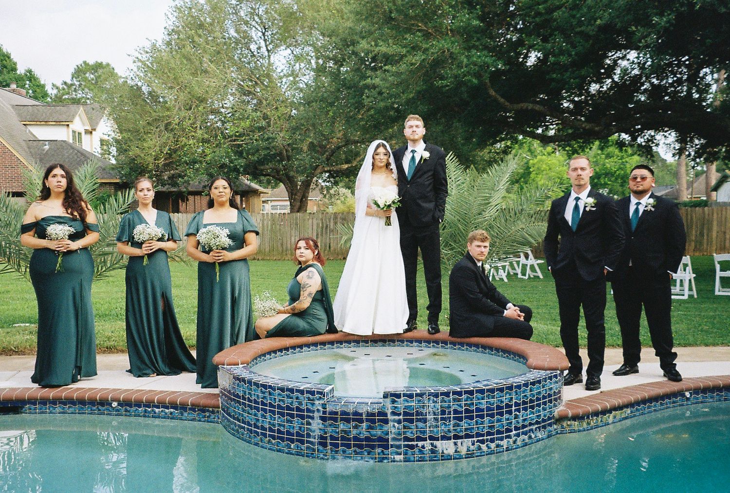 Wedding party poses by a pool fountain in emerald green and black formal attire.