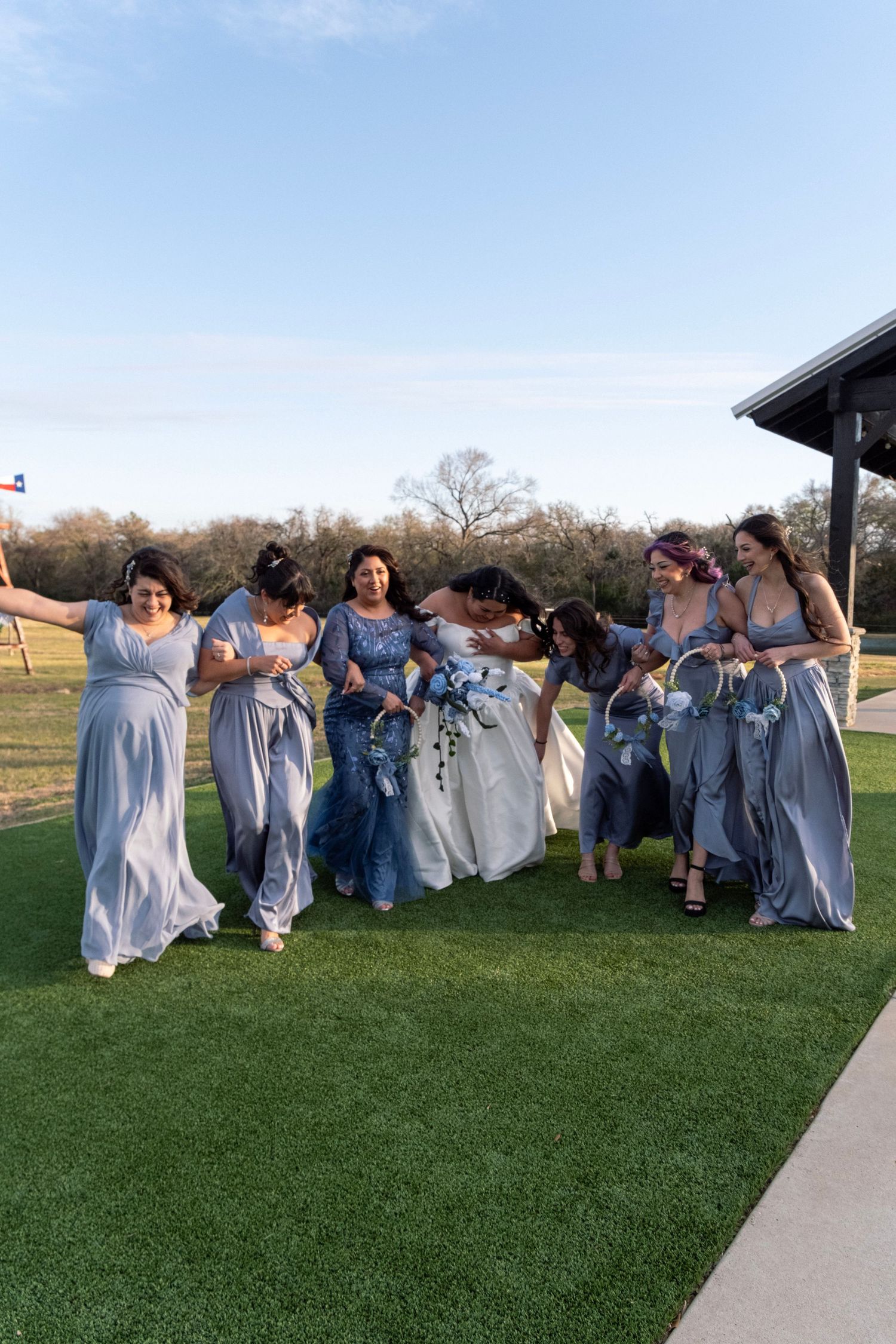 Bride in white gown celebrating with bridesmaids in light blue dresses on green lawn.
