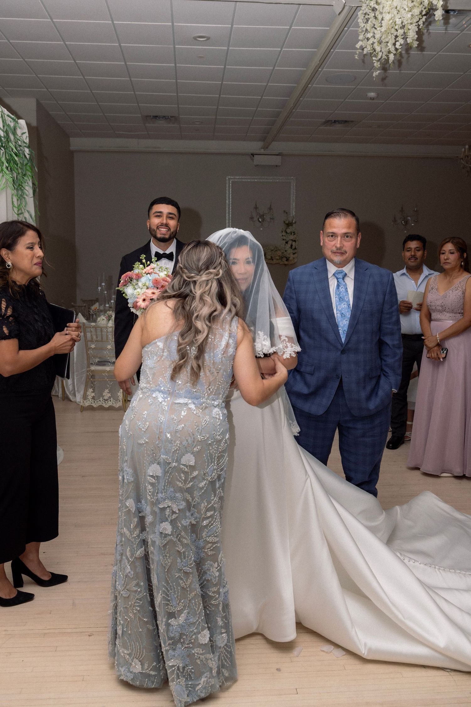 Bride in white gown with veil being greeted by family members during wedding ceremony entrance at elegant reception venue.