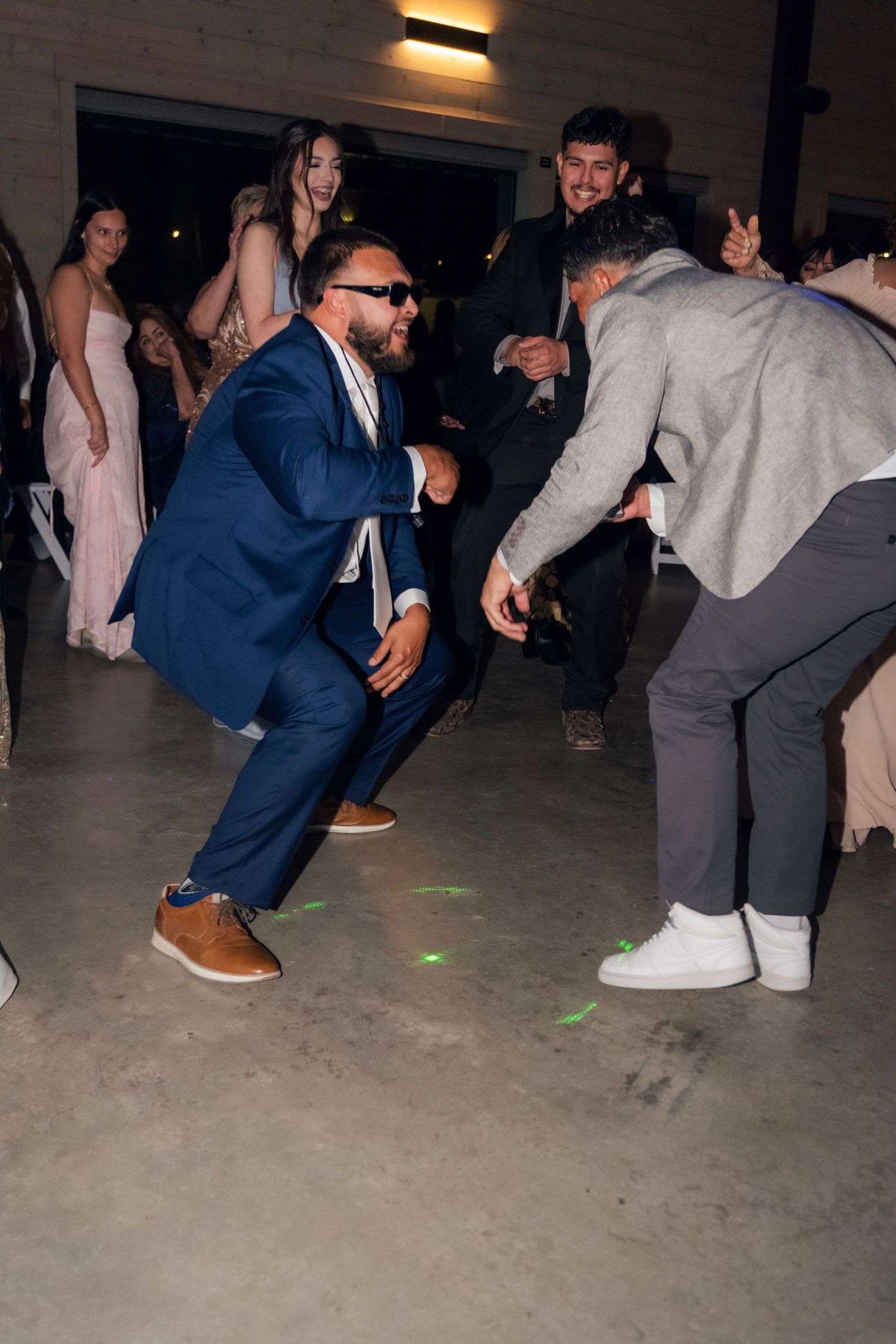 Wedding guest in blue suit dances energetically on reception dance floor with colorful laser lights.