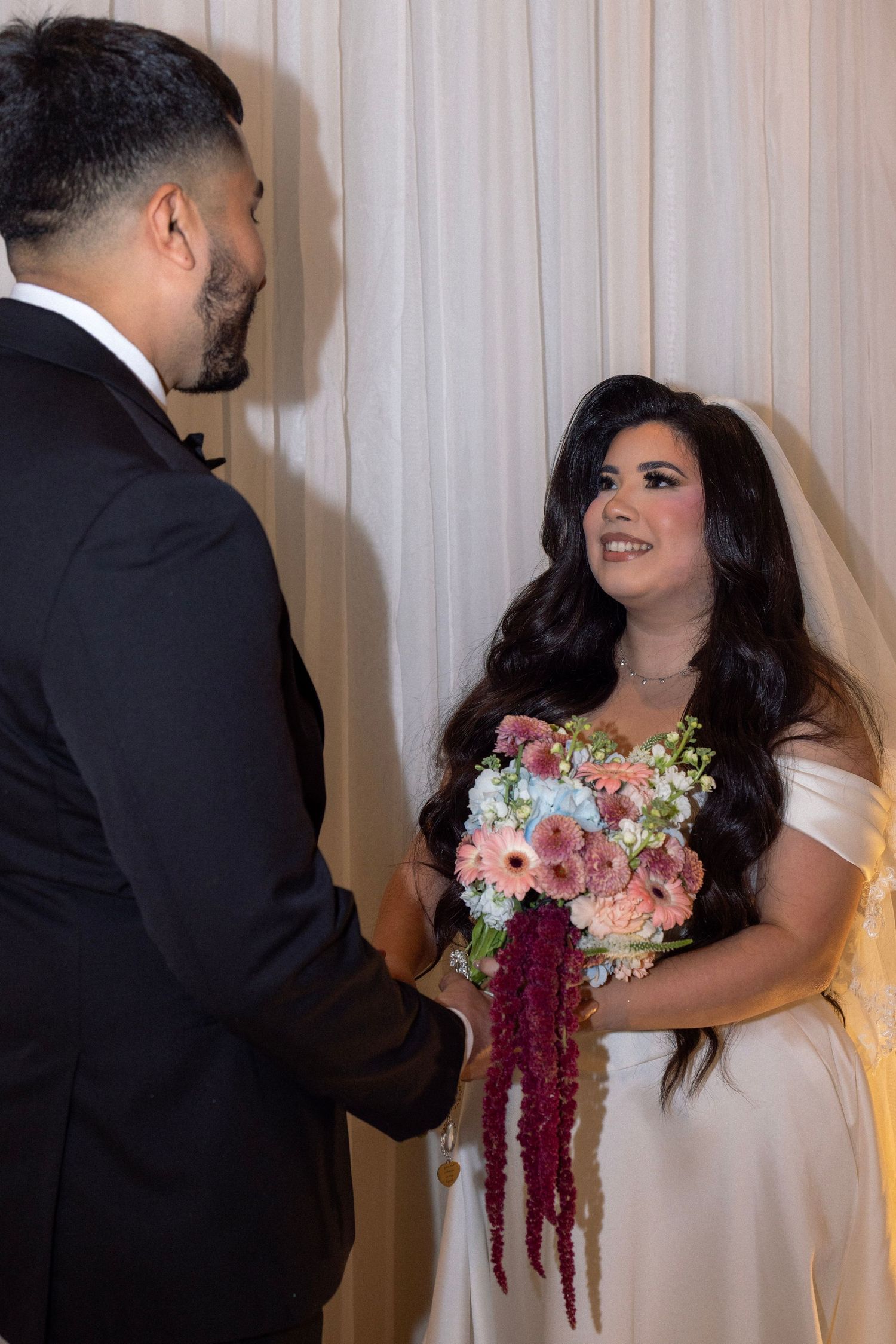 Bride holding colorful bouquet exchanges vows with groom in black suit at elegant wedding ceremony.