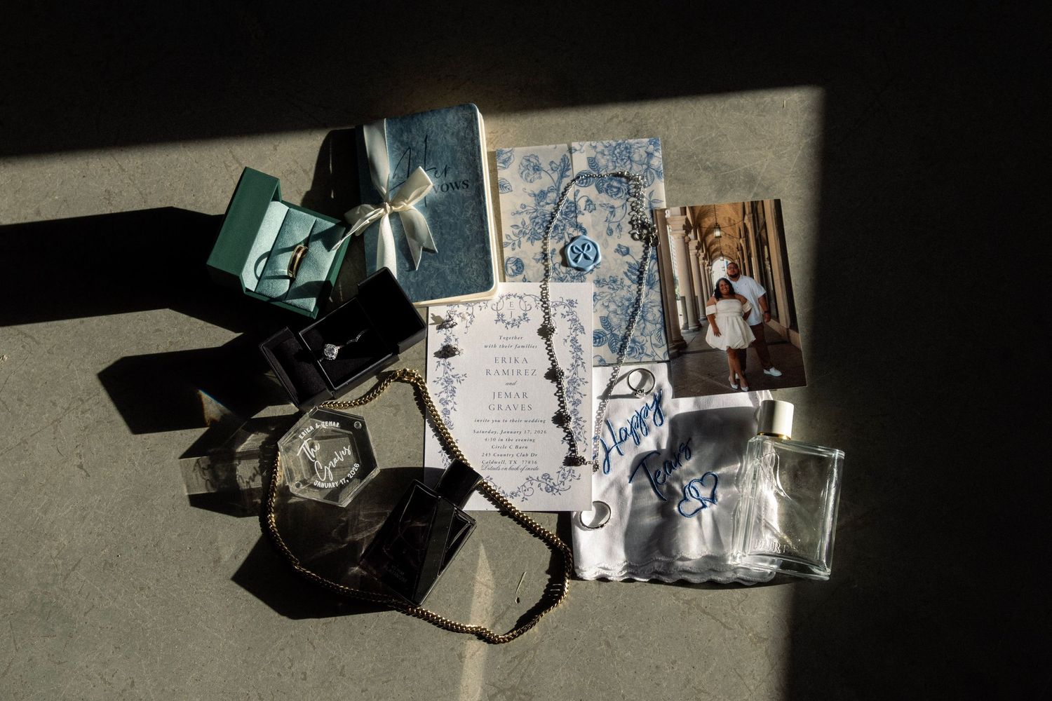 Flat lay of wedding stationery, photos, rings, and accessories arranged in natural sunlight.