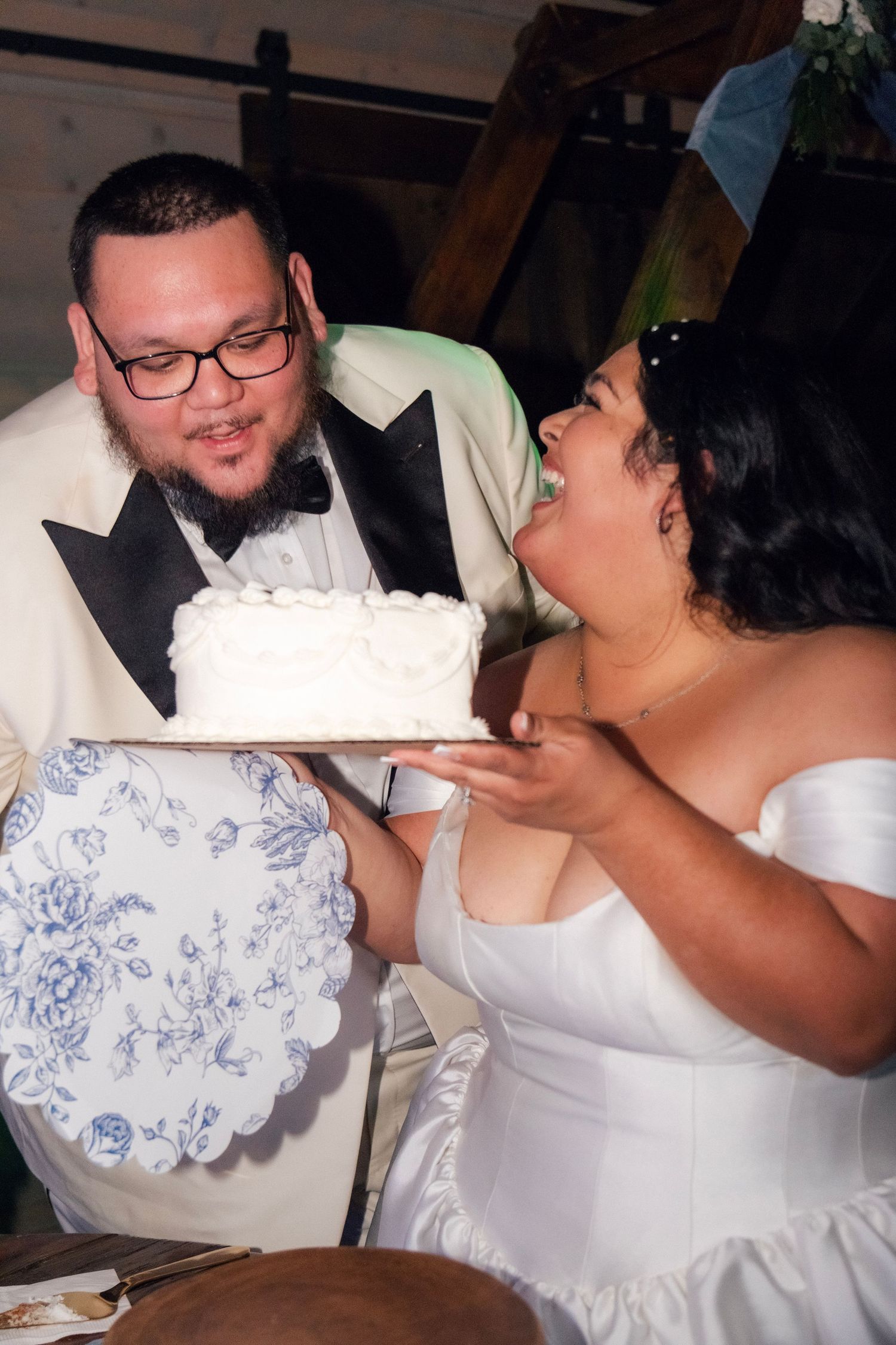 Bride and groom admire white wedding cake on decorative blue floral plate at reception.