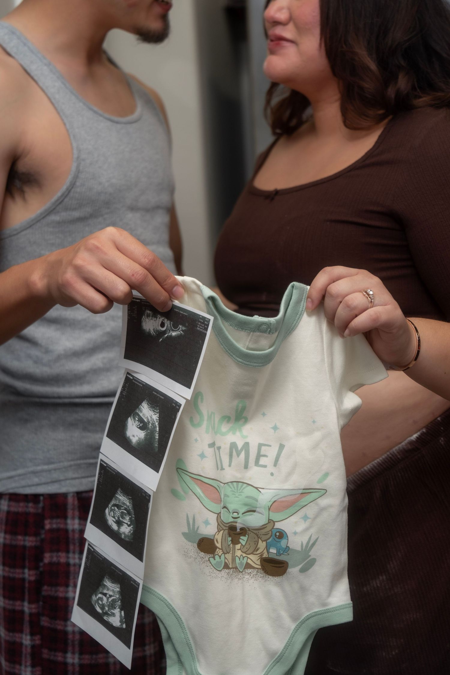 Couple holds Baby Yoda onesie and ultrasound photos for Star Wars themed pregnancy reveal.