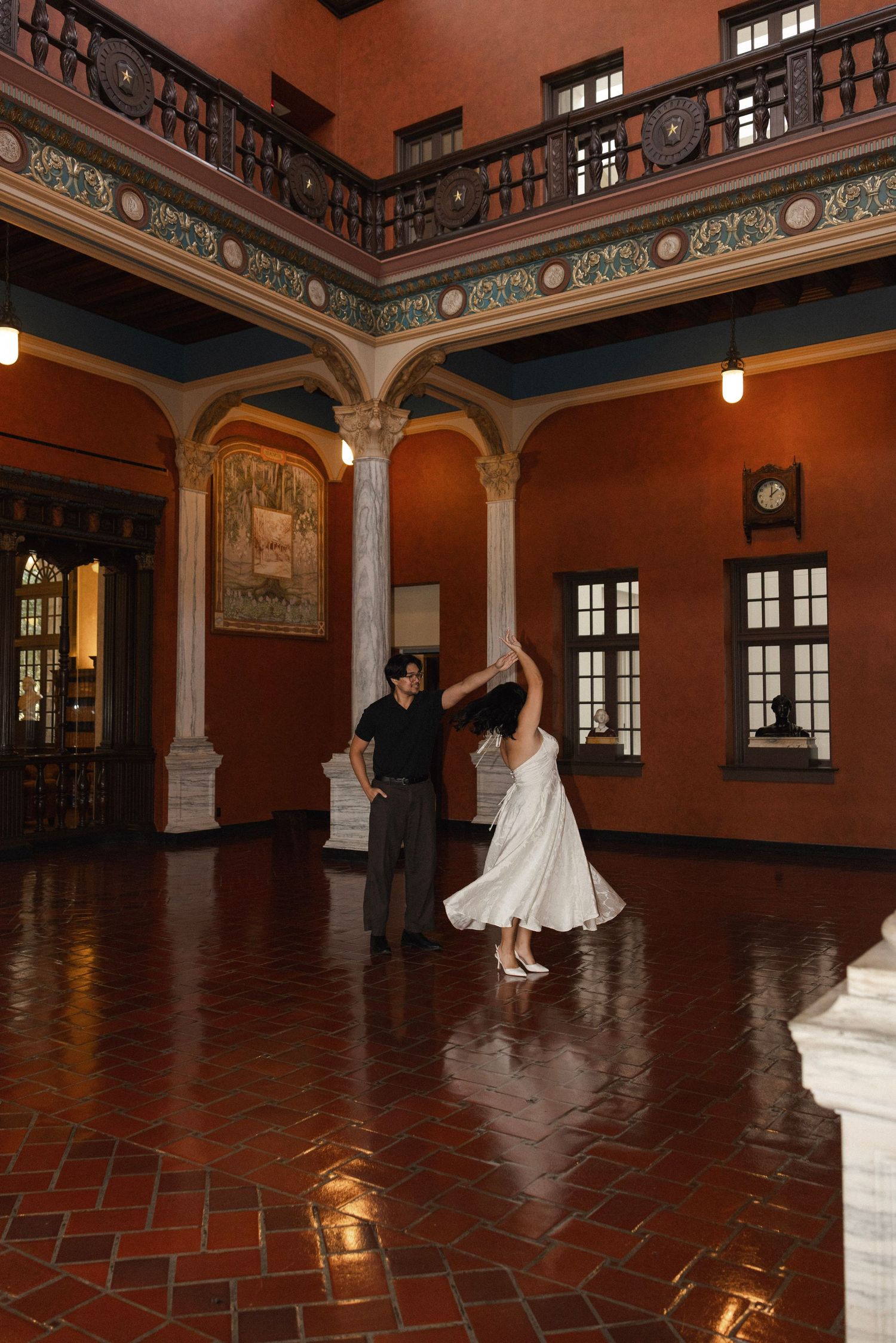 Couple dancing elegantly in a grand historic ballroom with terracotta floors and ornate colonial architecture.