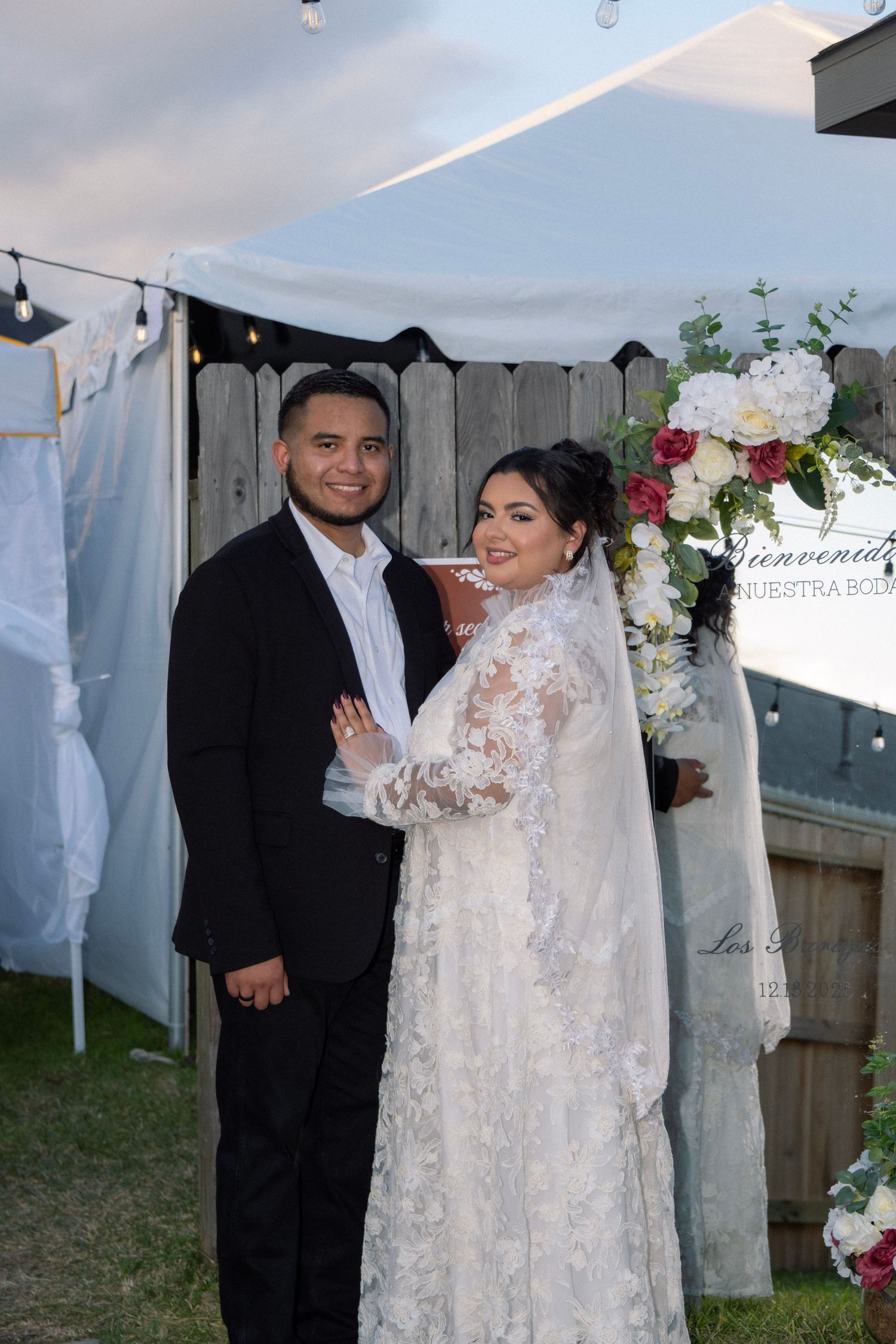 Smiling bride and groom posing together under white tent at outdoor backyard wedding ceremony.