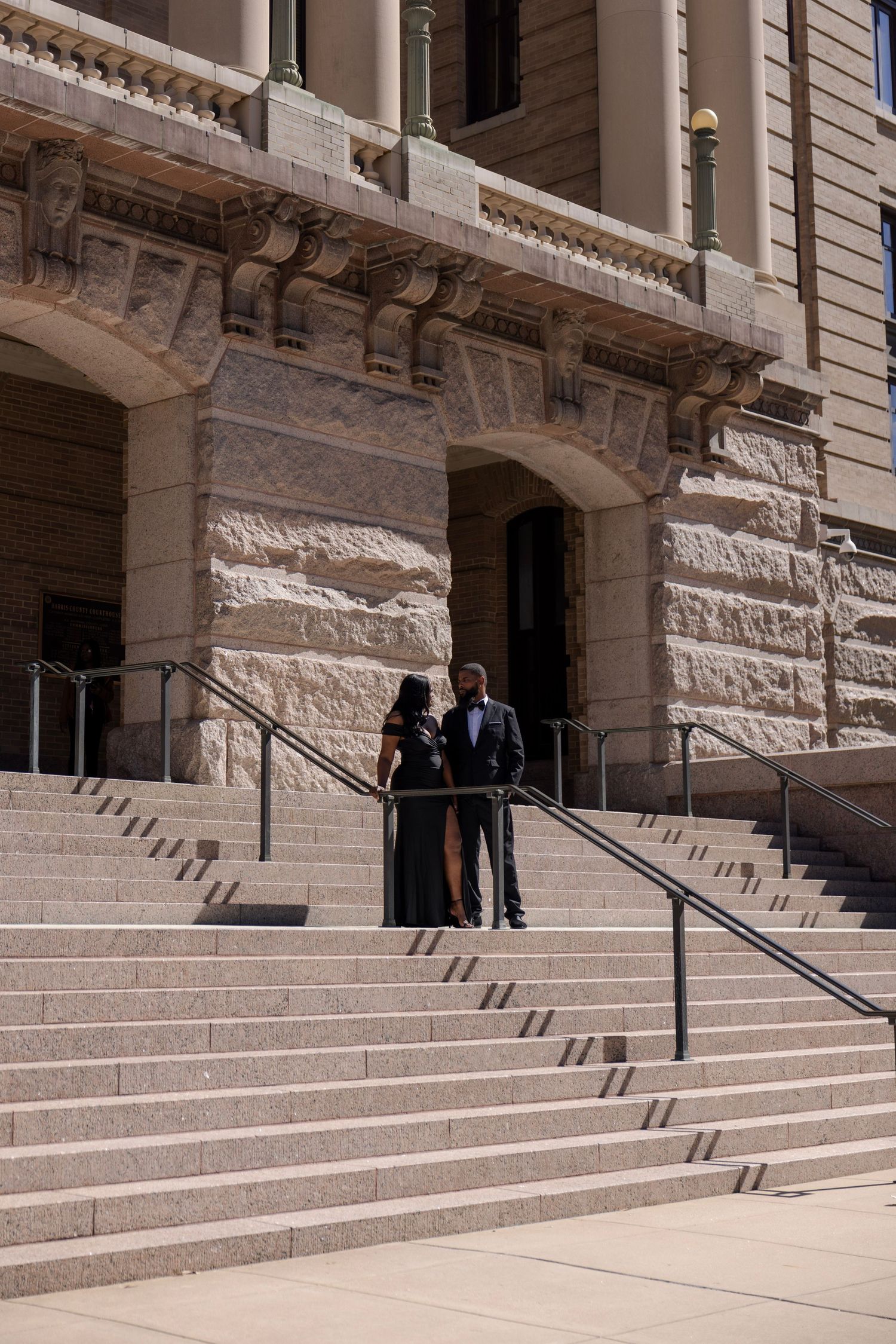 Elegant couple in formal attire posing on grand stone steps of a historic courthouse building.