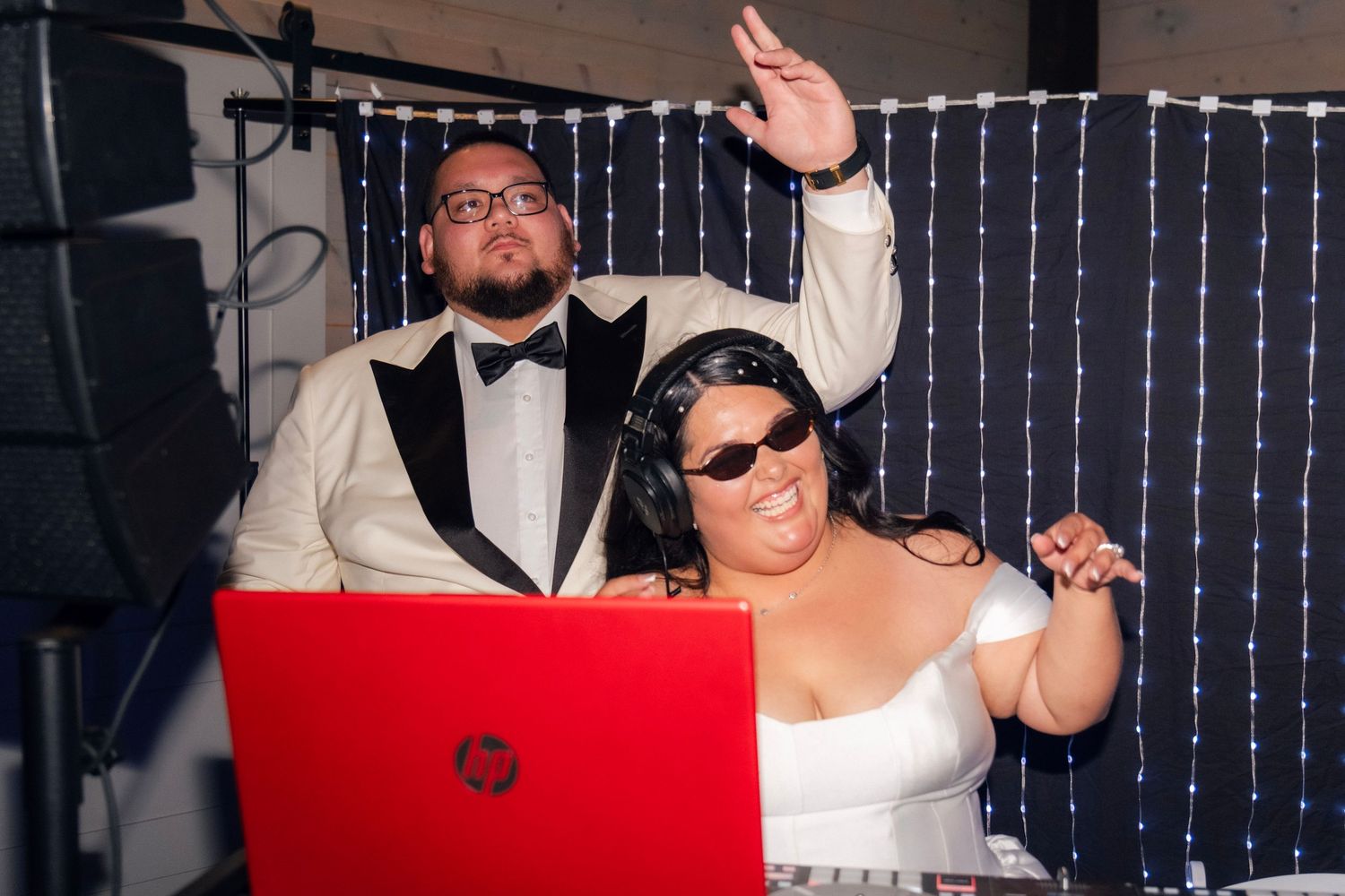 Bride and groom pose together behind red DJ laptop at wedding reception photo booth.