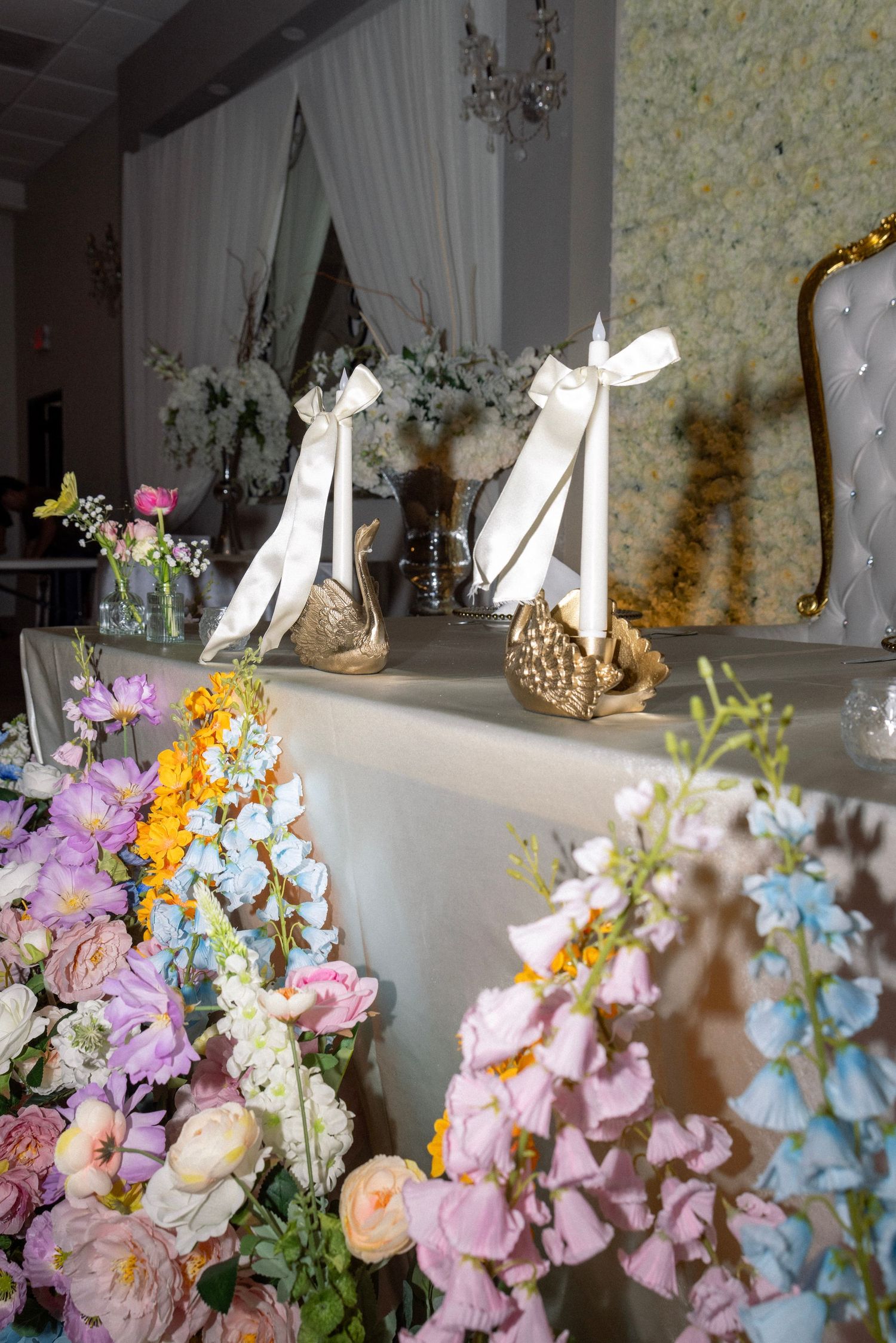 Elegant wedding reception table decorated with colorful flowers and golden swan figurines with white bows.