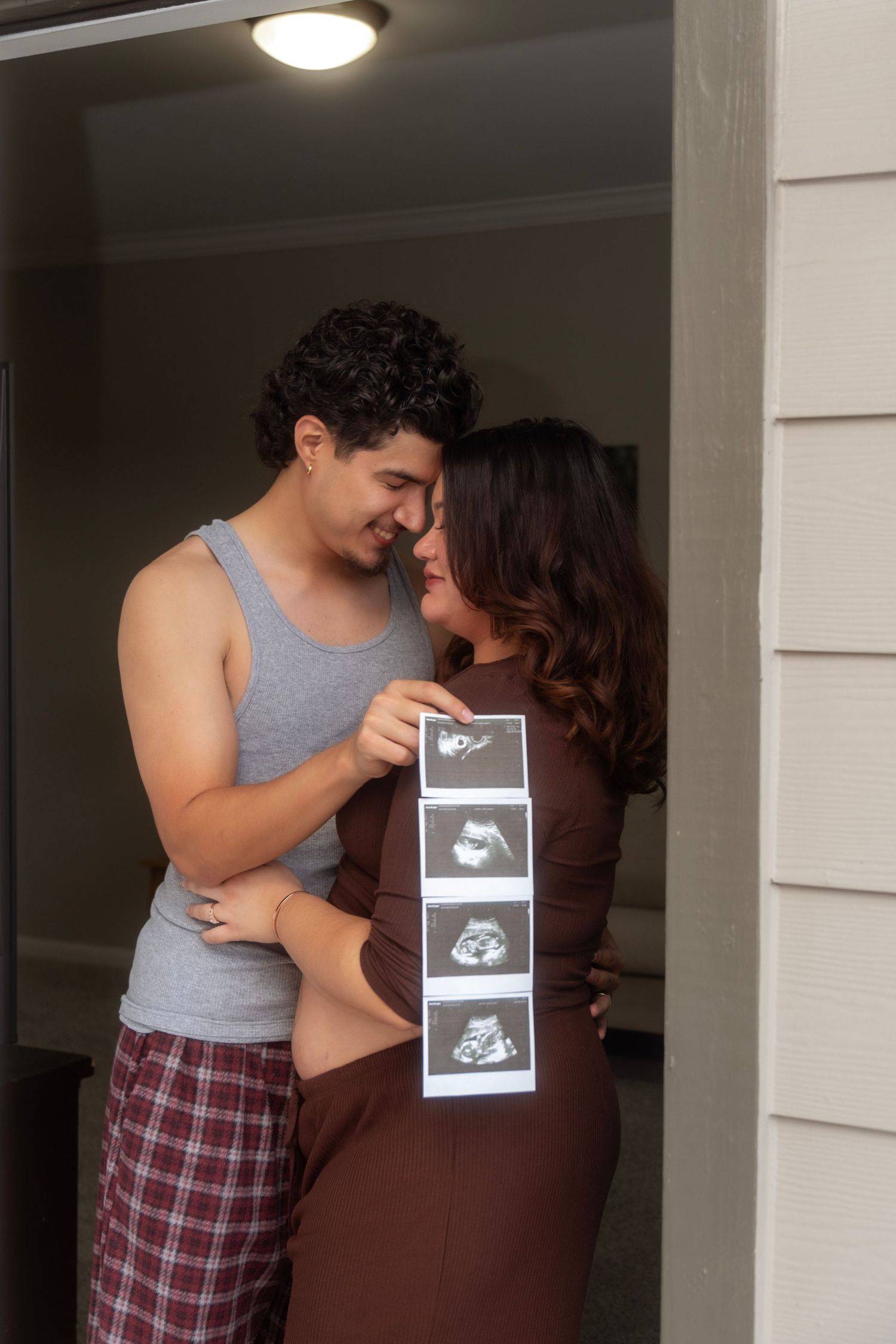 Expecting couple shares tender moment holding ultrasound photos in home doorway.