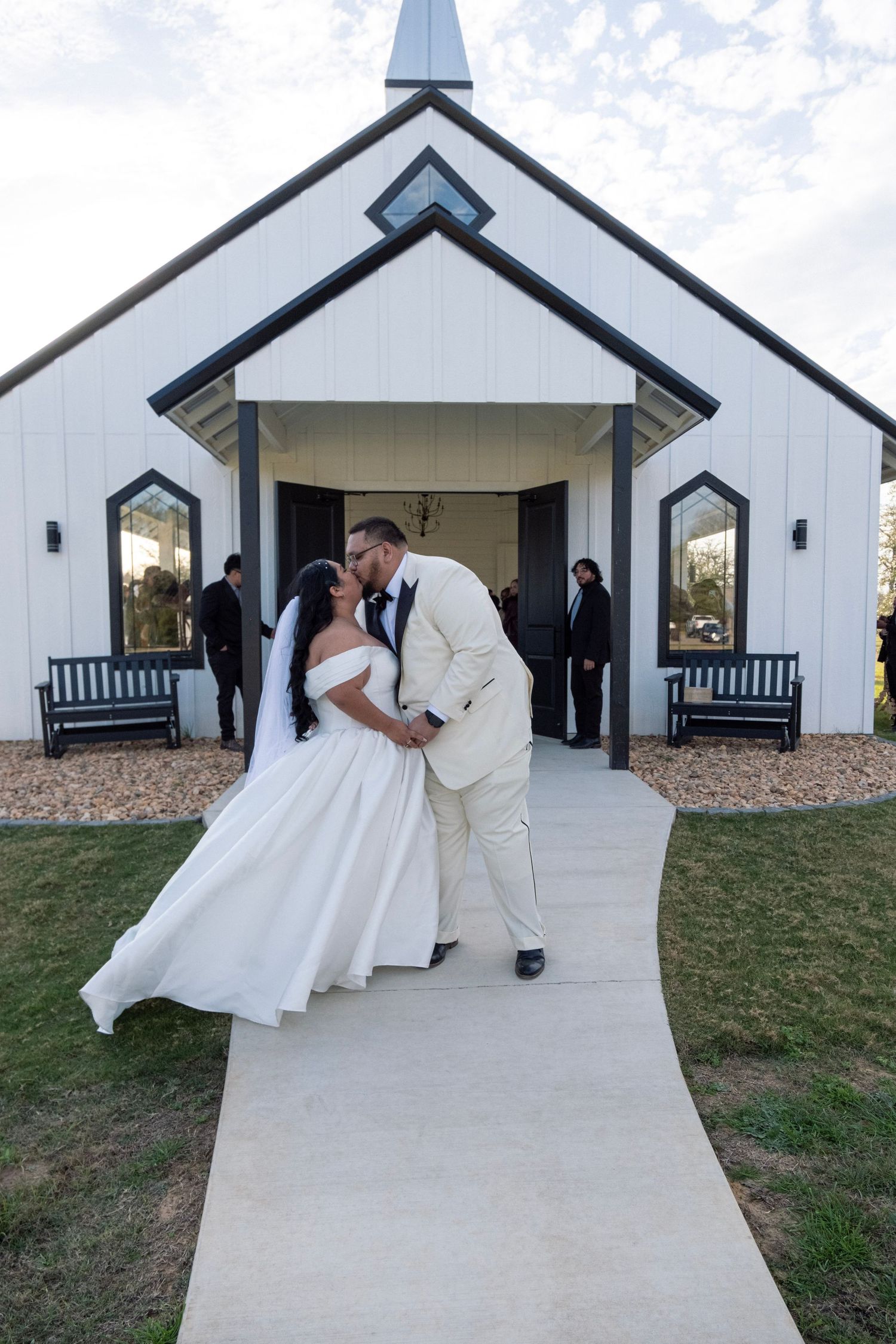 Bride and groom sharing a kiss on the pathway outside a white chapel wedding venue after their ceremony.