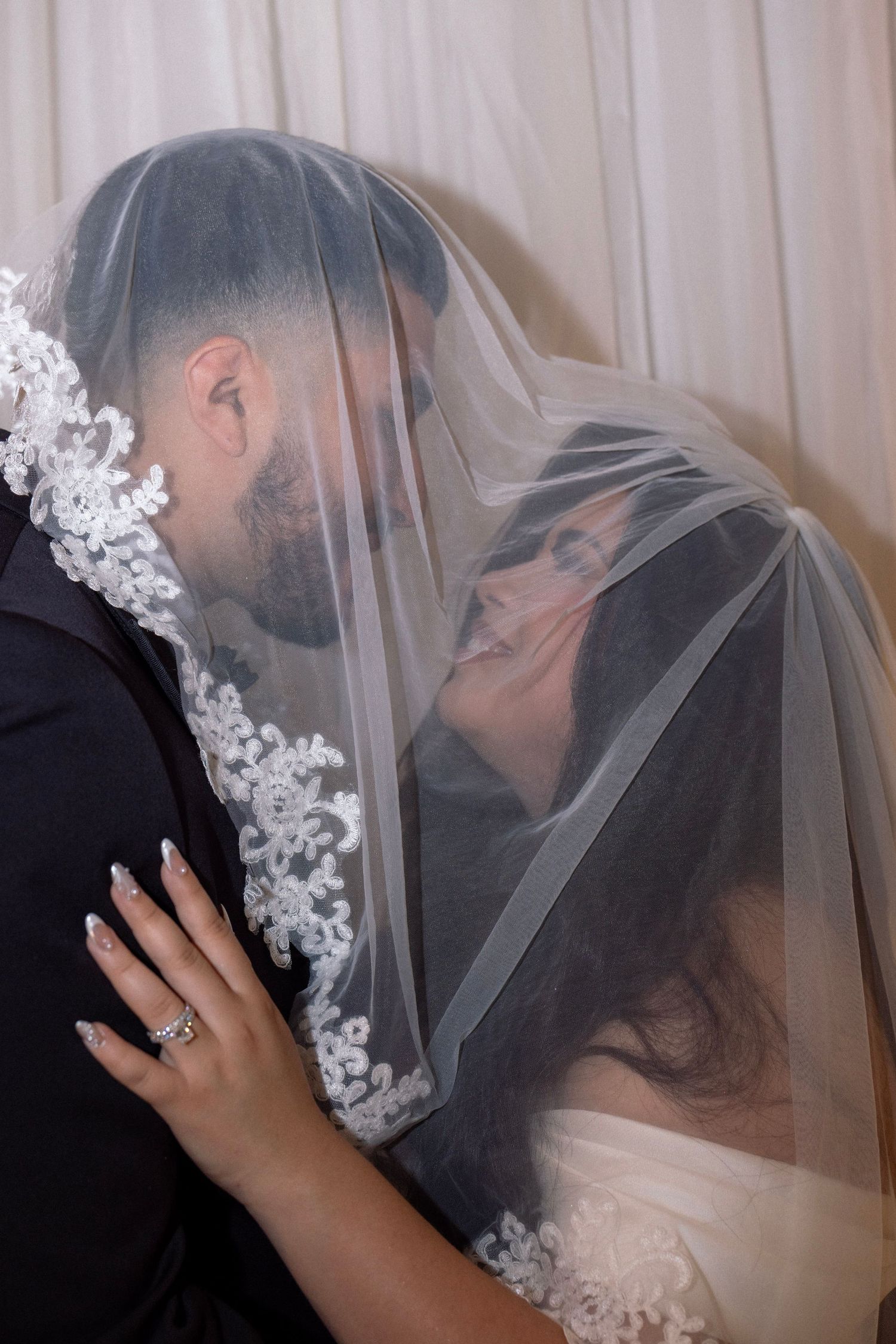 Bride and groom share romantic kiss under lace-trimmed wedding veil at their reception.
