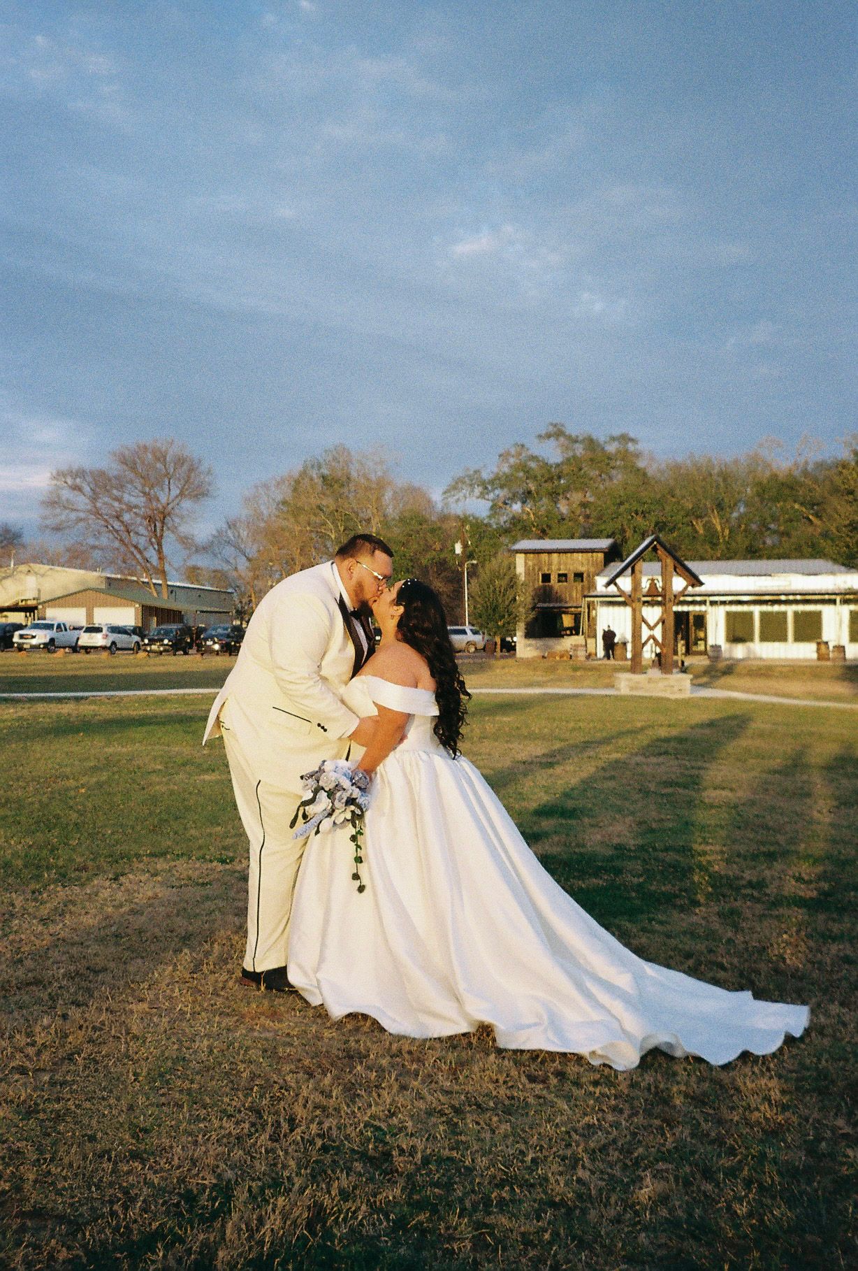 Bride and groom sharing a romantic dip kiss at golden hour on a green lawn.
