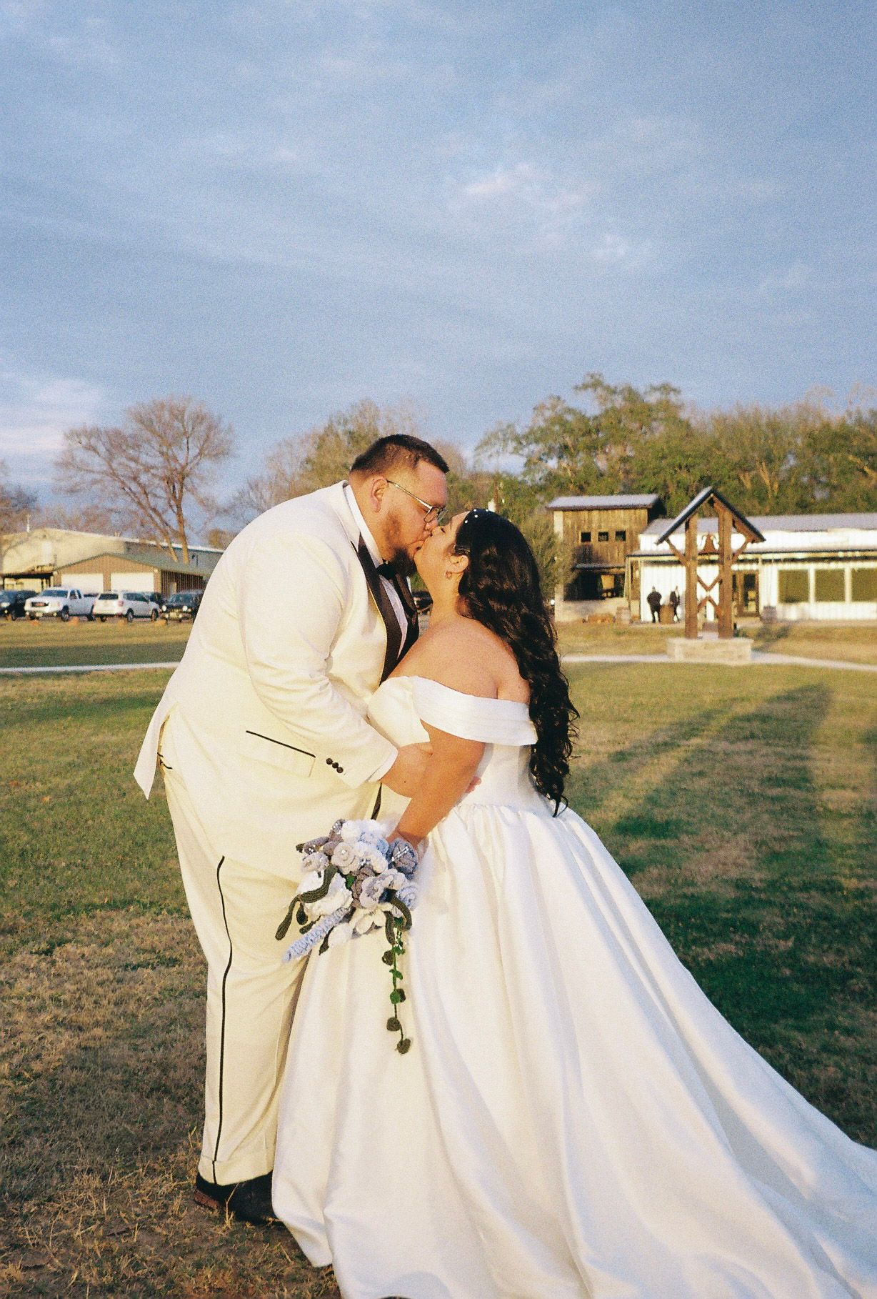 Newlywed couple sharing a romantic kiss outdoors in a rustic wedding venue setting.