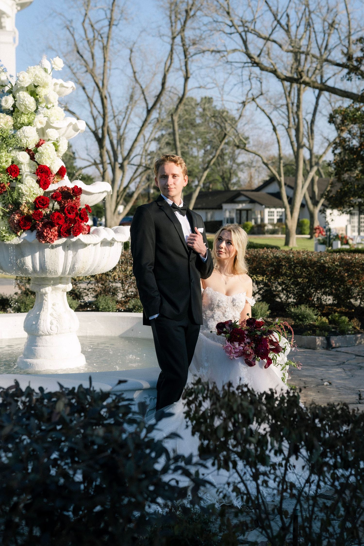 Bride and groom pose outdoors near white floral urn with red and white flowers during winter wedding ceremony.