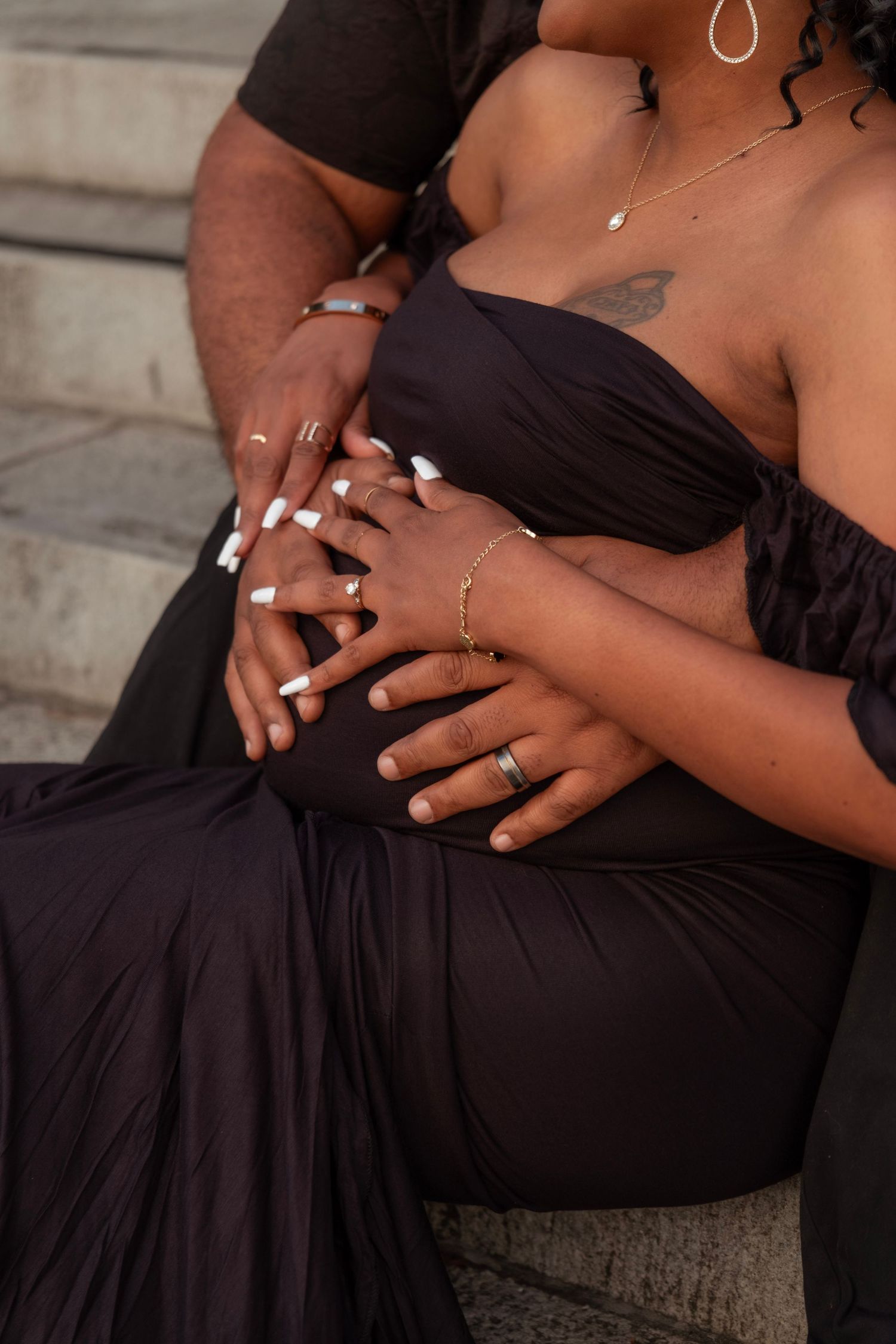 Close-up of couple's hands tenderly cradling pregnant belly in elegant black maternity dress.