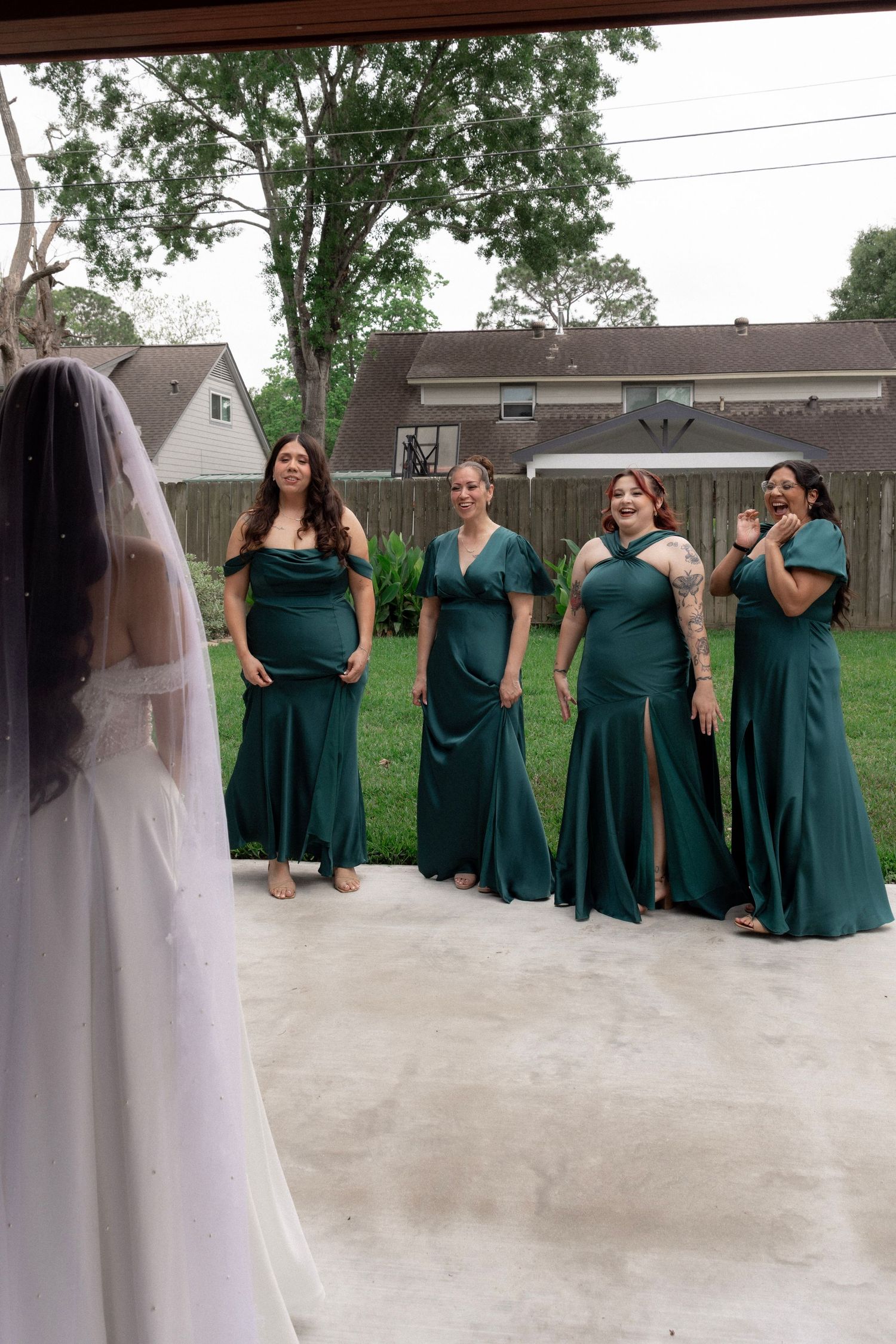 Bridesmaids in green dresses react with joy seeing the bride for the first time.