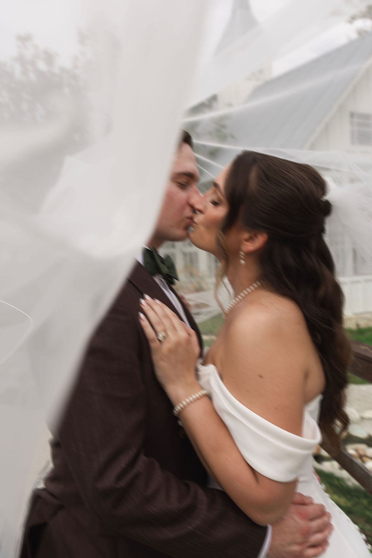 Bride and groom sharing a romantic kiss framed by flowing white veil on their wedding day.