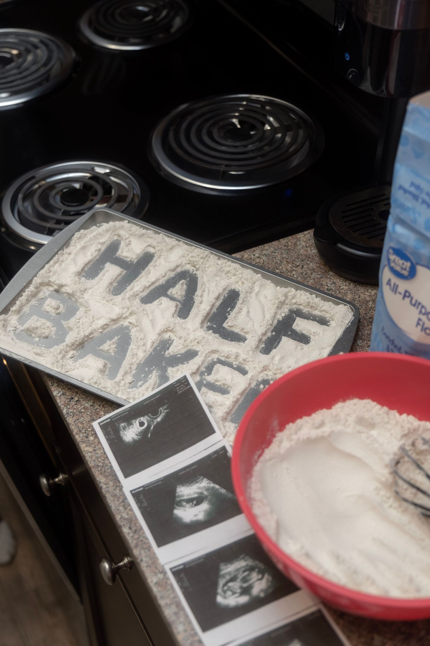 Baking pan with flour spelling Half Baked beside ultrasound photos for pregnancy announcement.