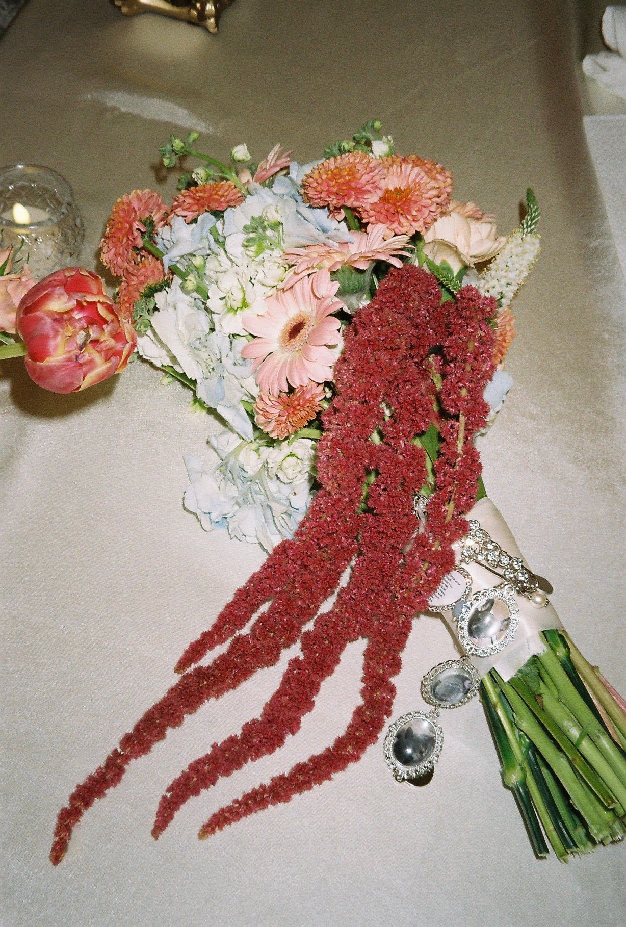 Wedding bouquet with pink gerberas, hydrangeas, and cascading red amaranthus rests on white tablecloth.