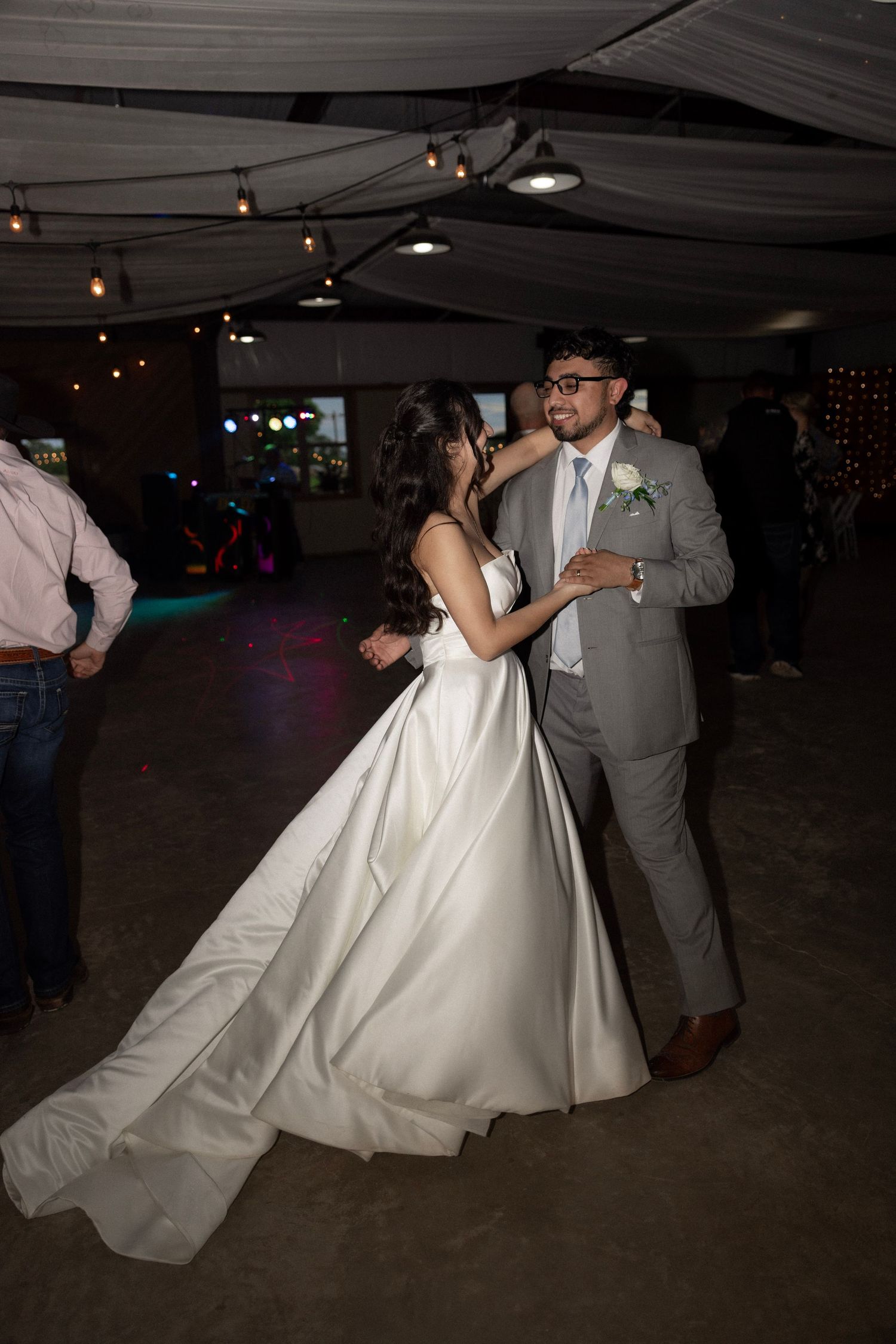 Bride and groom share first dance under string lights at elegant indoor wedding reception venue.
