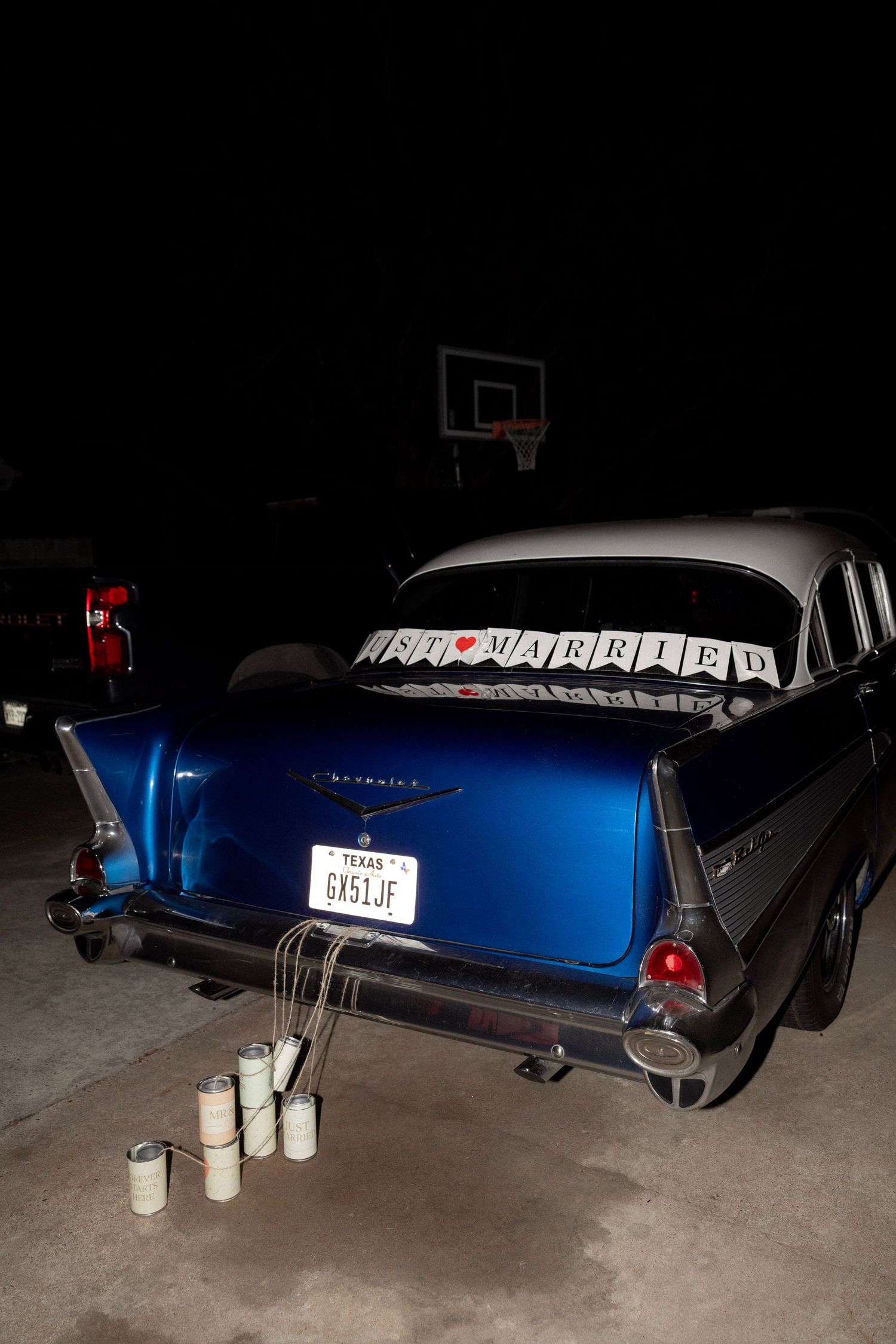 Classic blue 1957 Chevrolet just married getaway car with tin cans at night.