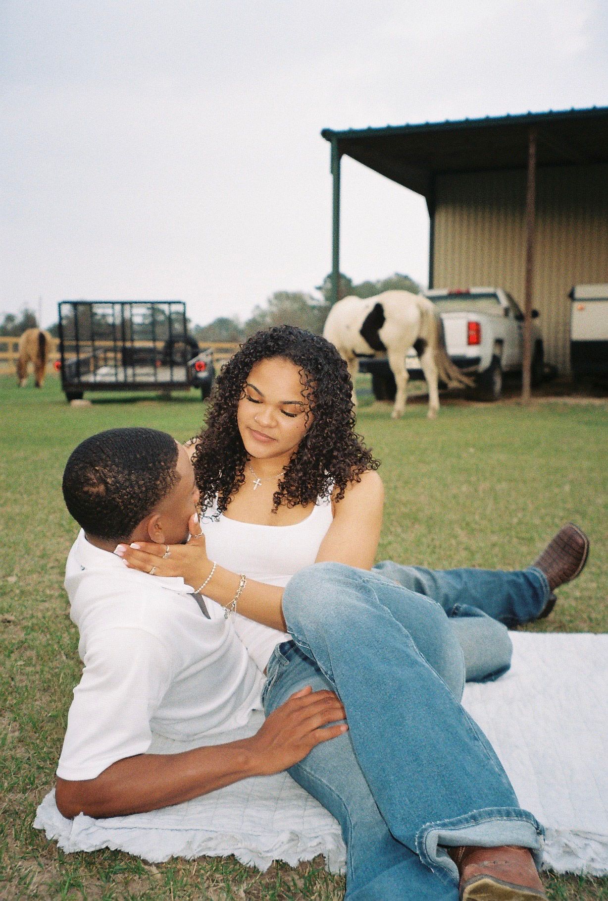 Couple relaxing together on a blanket outdoors with horses grazing nearby.