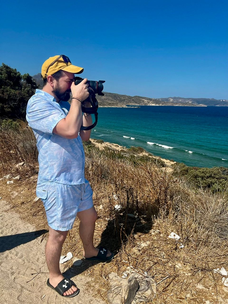 Bearded photographer captures ocean landscape with DSLR camera on scenic coastal trail.