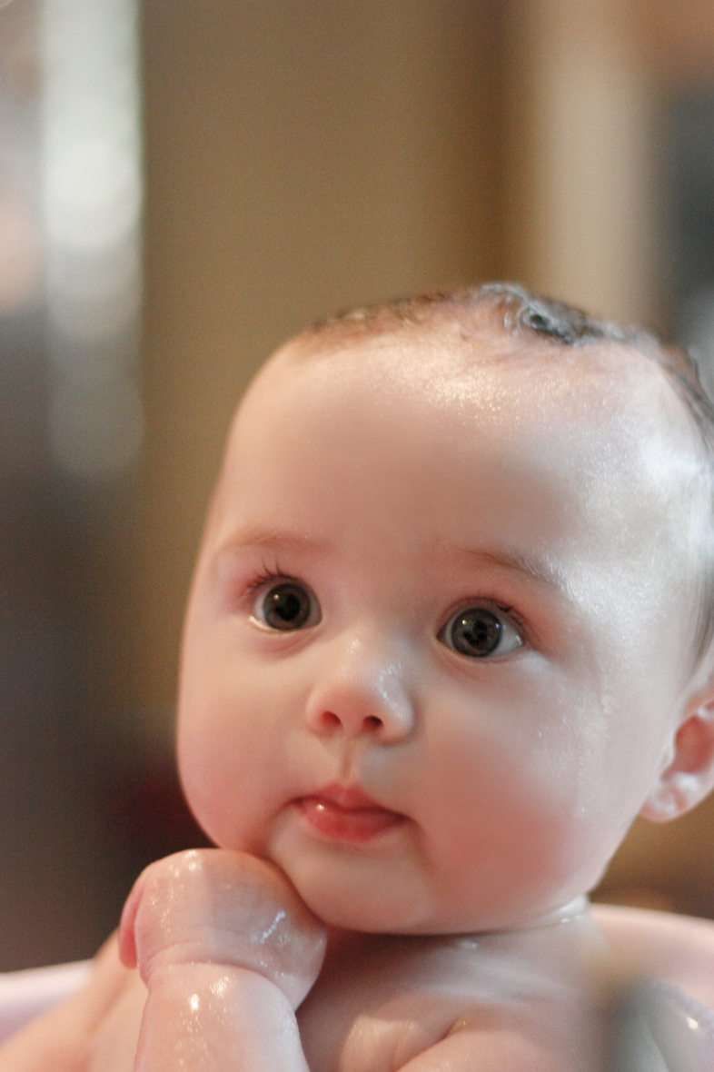 Close-up of a wet baby being bathed, looking up with wide curious eyes.