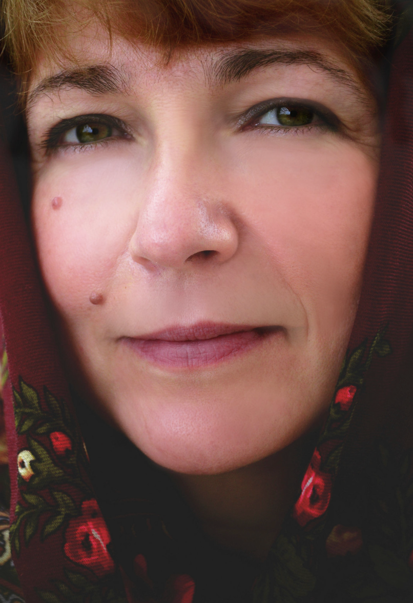 Close-up portrait of a woman with green eyes and a mole, wearing a floral red scarf.