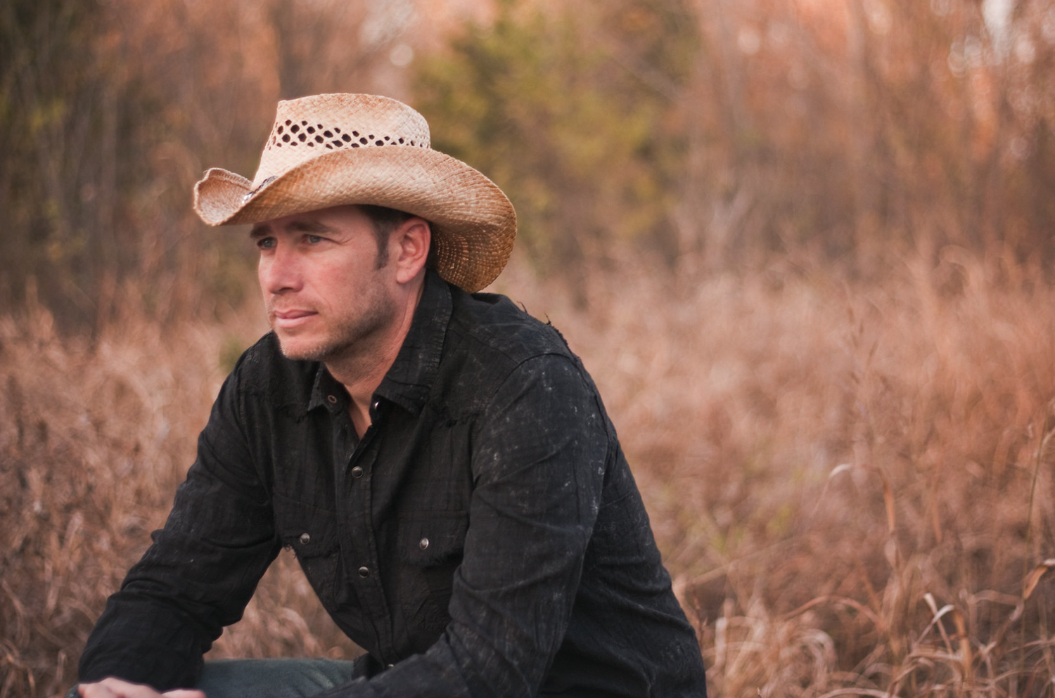 Man in a cowboy hat sitting in a golden field during autumn.