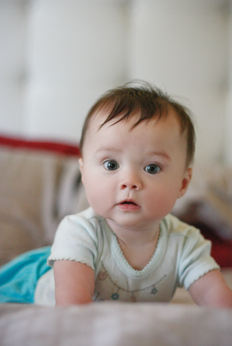 Curious baby with blue eyes doing tummy time on a soft surface indoors.