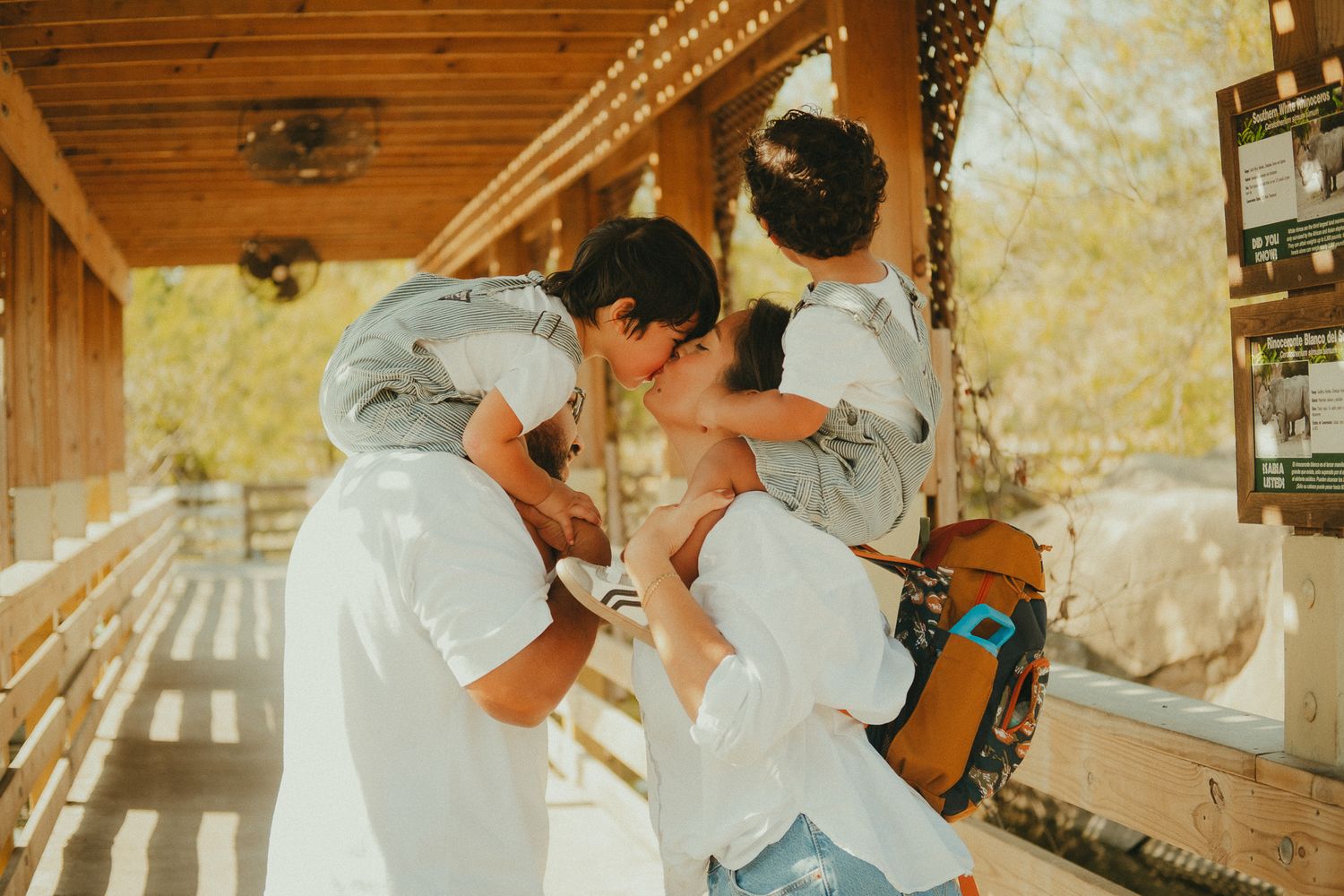 Couple sharing a kiss while holding their child on a sunny wooden porch.