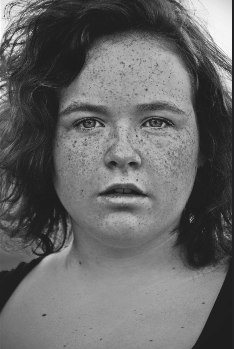 Black and white close-up portrait of a young freckled woman with curly hair.