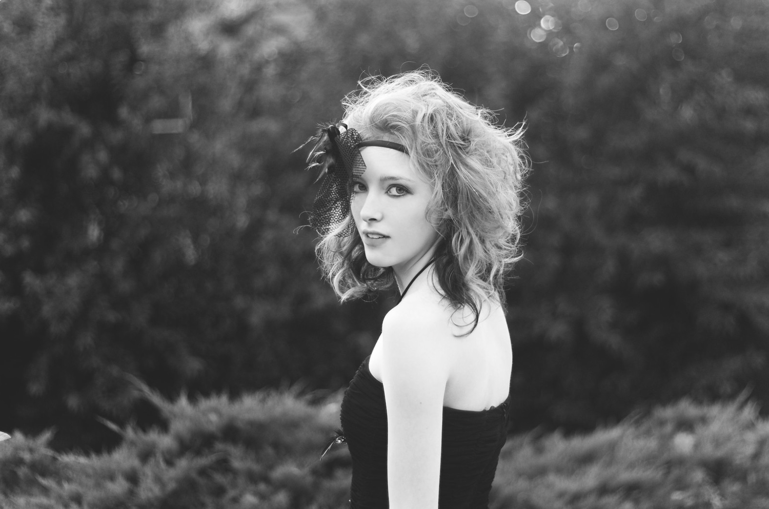 Black and white photo of a young woman with curly hair outdoors.