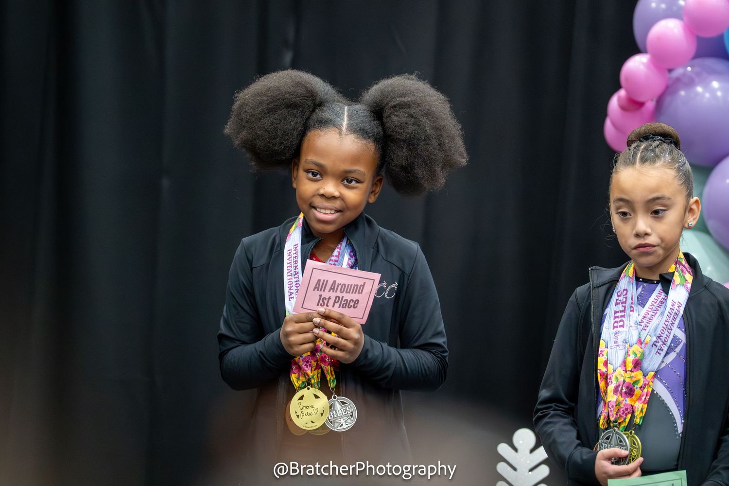 Young gymnast proudly holds All-Around 1st Place award with gold medal at gymnastics competition. bratcher photography and houston photograp